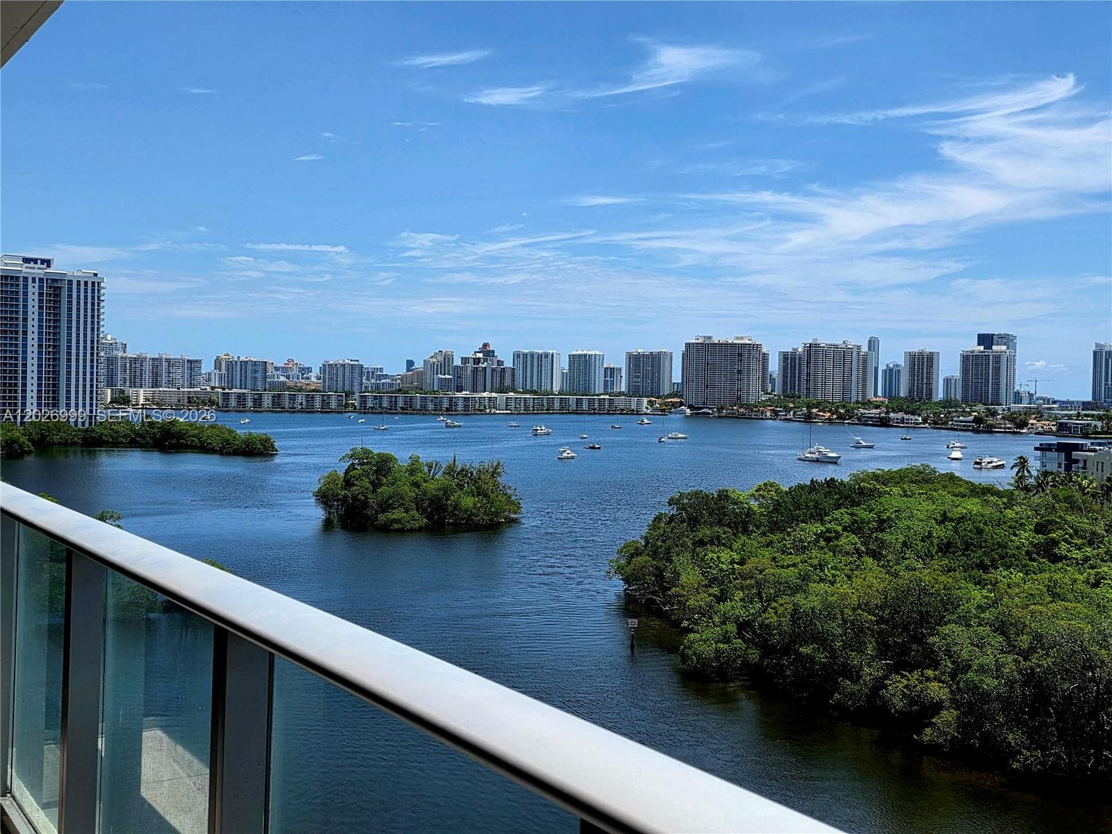 Spacious balcony with glass railings and sweeping views over the waterway, treetops, and skyline. The long outdoor area extends the living space with a scenic backdrop.