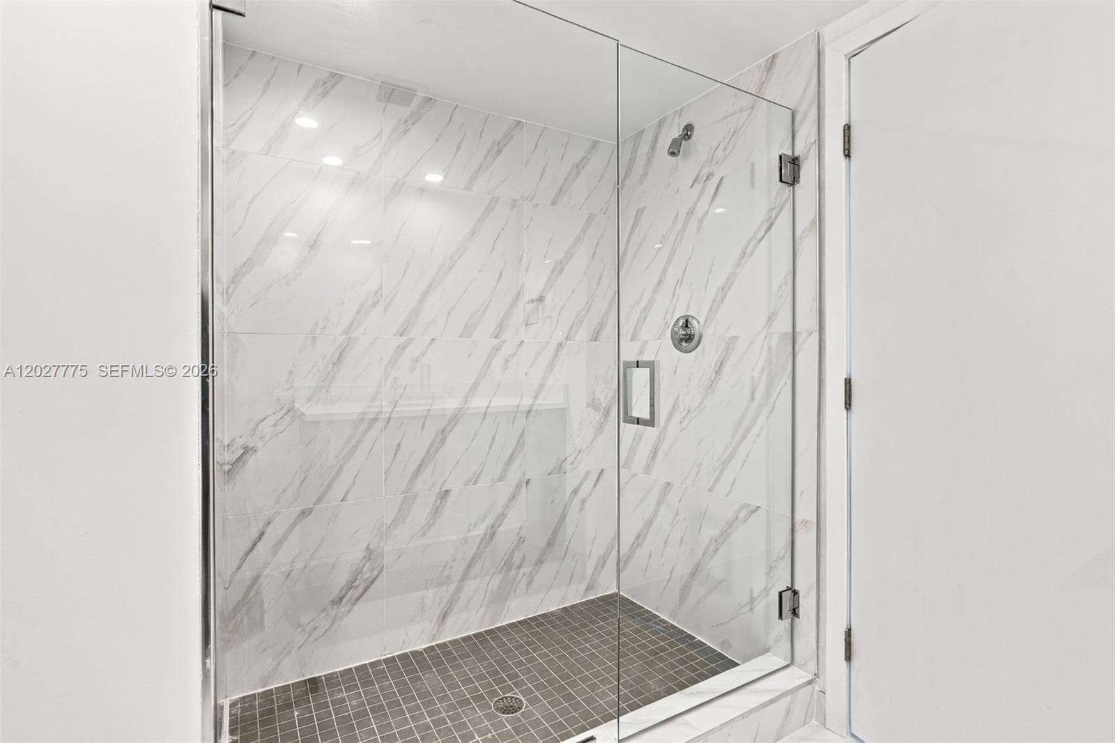 Glass-enclosed shower featuring white marble-patterned tile, a dark gray mosaic tile floor, and a built-in shower niche