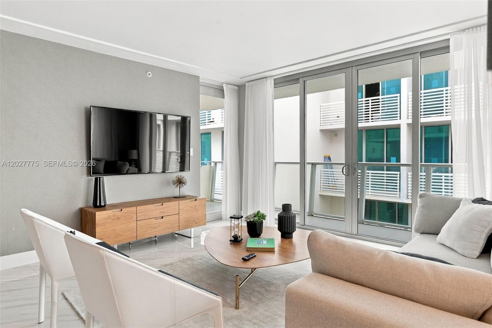 Sliding glass doors with sheer drapery, wood-finish console with storage, mounted flat-panel television, and light-tone flooring