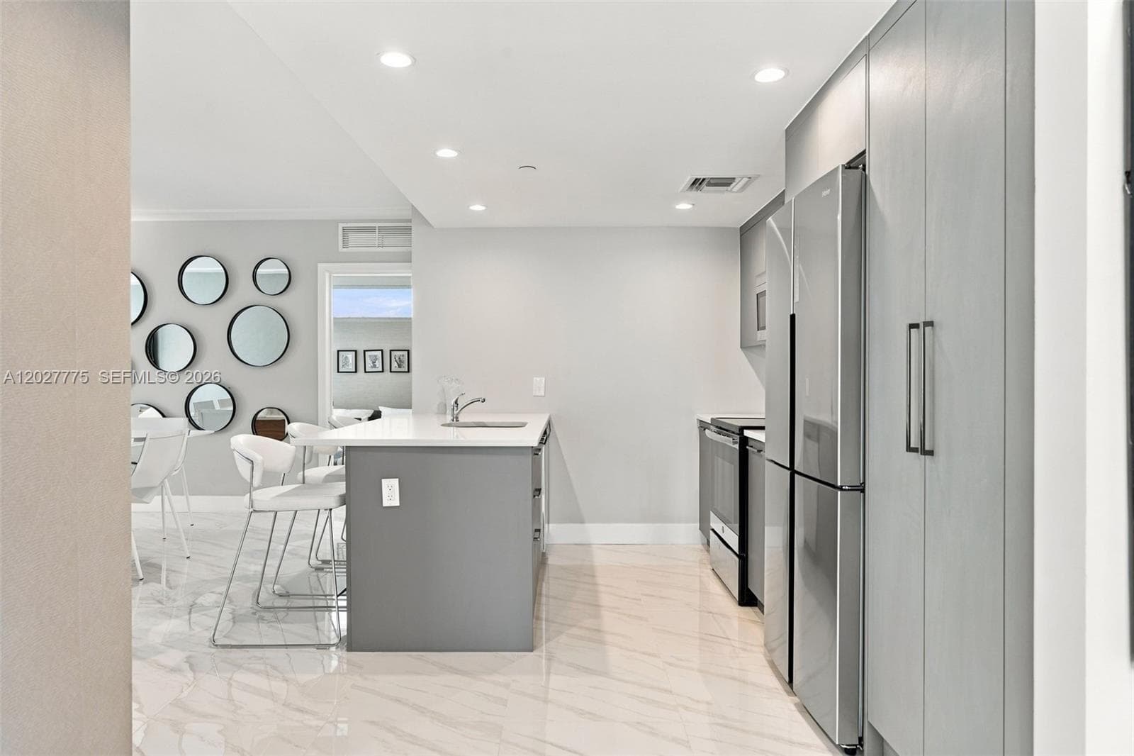 Kitchen featuring an island with a built-in sink, recessed lighting, sleek gray cabinetry, stainless steel appliances, and large format floor tiling
