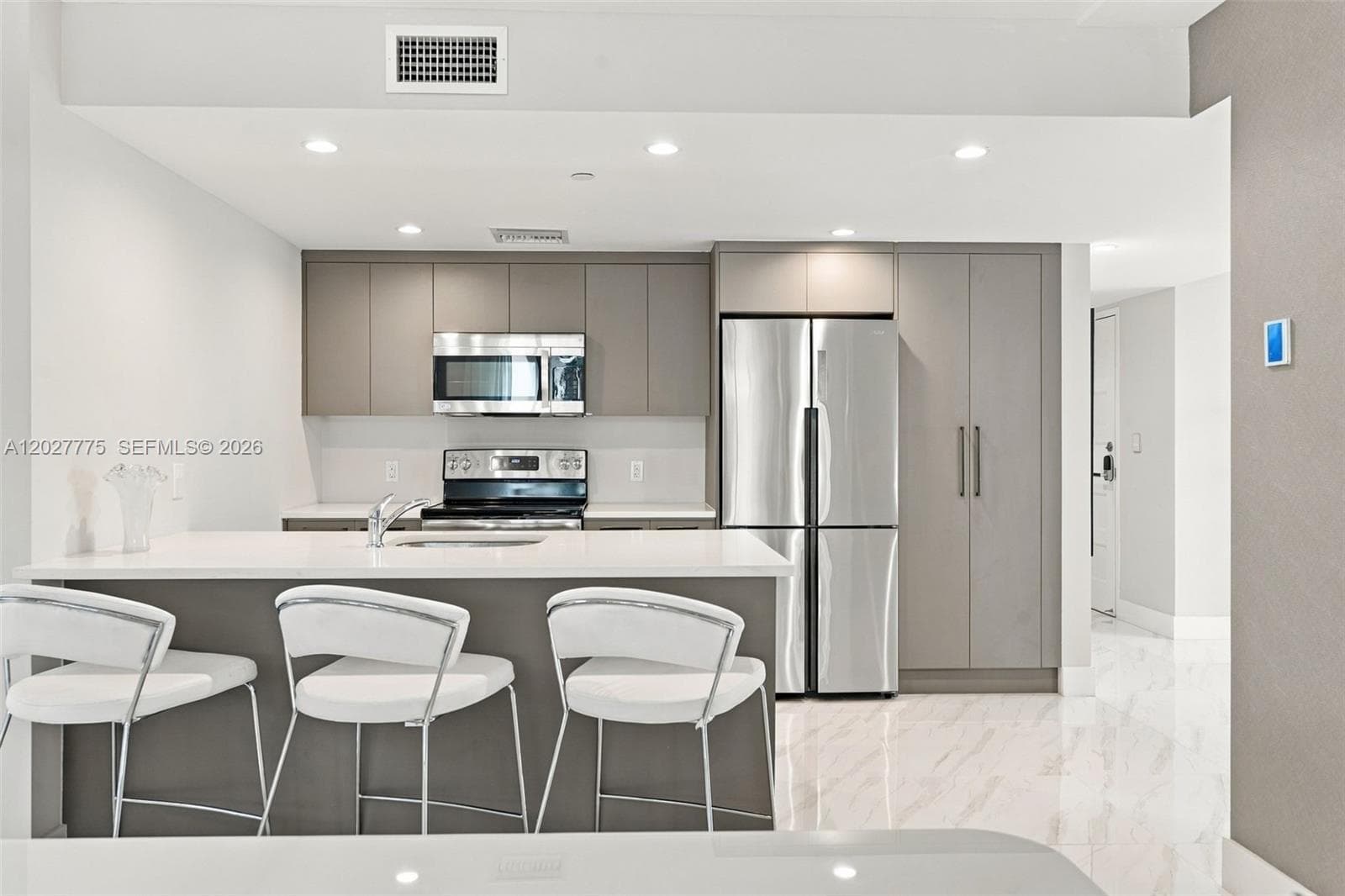 Modern kitchen featuring stainless steel appliances, recessed lighting, sleek gray cabinetry, a white countertop island, and white tile flooring