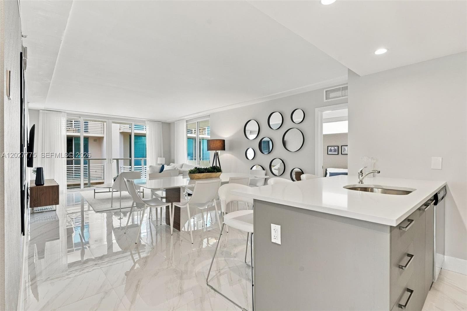 Open-concept living space with large format tile flooring, a kitchen island with integrated sink, and an expansive balcony