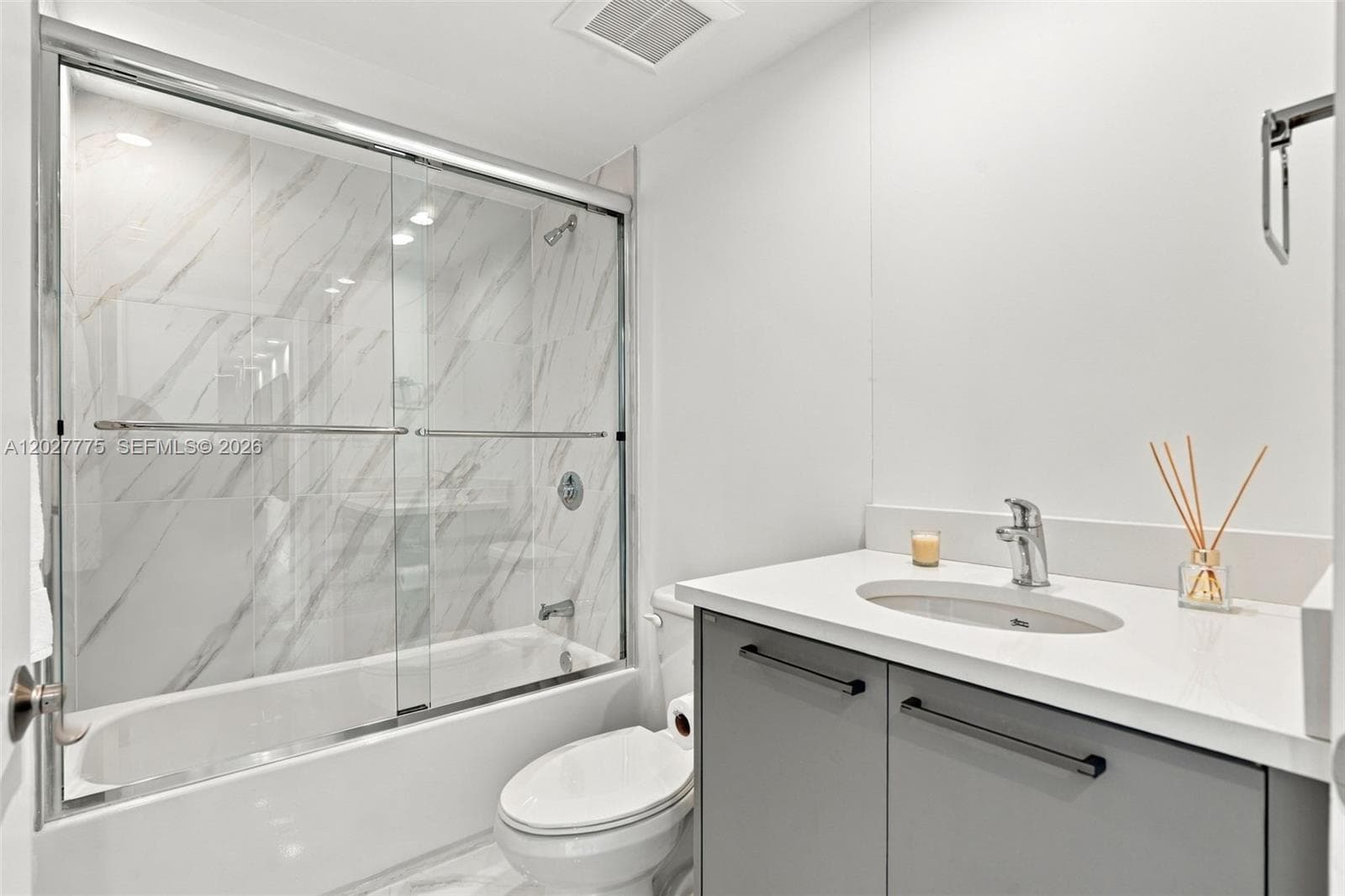 Bathtub with sliding glass enclosure, marble-style wall tiling, and a vanity with a white countertop and undermount sink