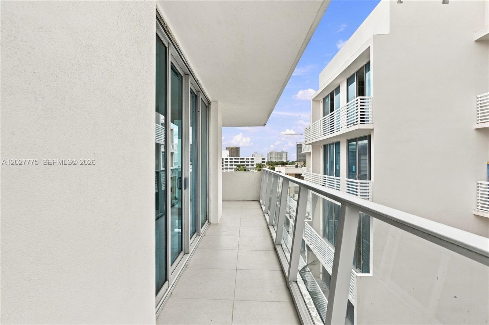 Elongated outdoor balcony featuring tile flooring and a glass railing
