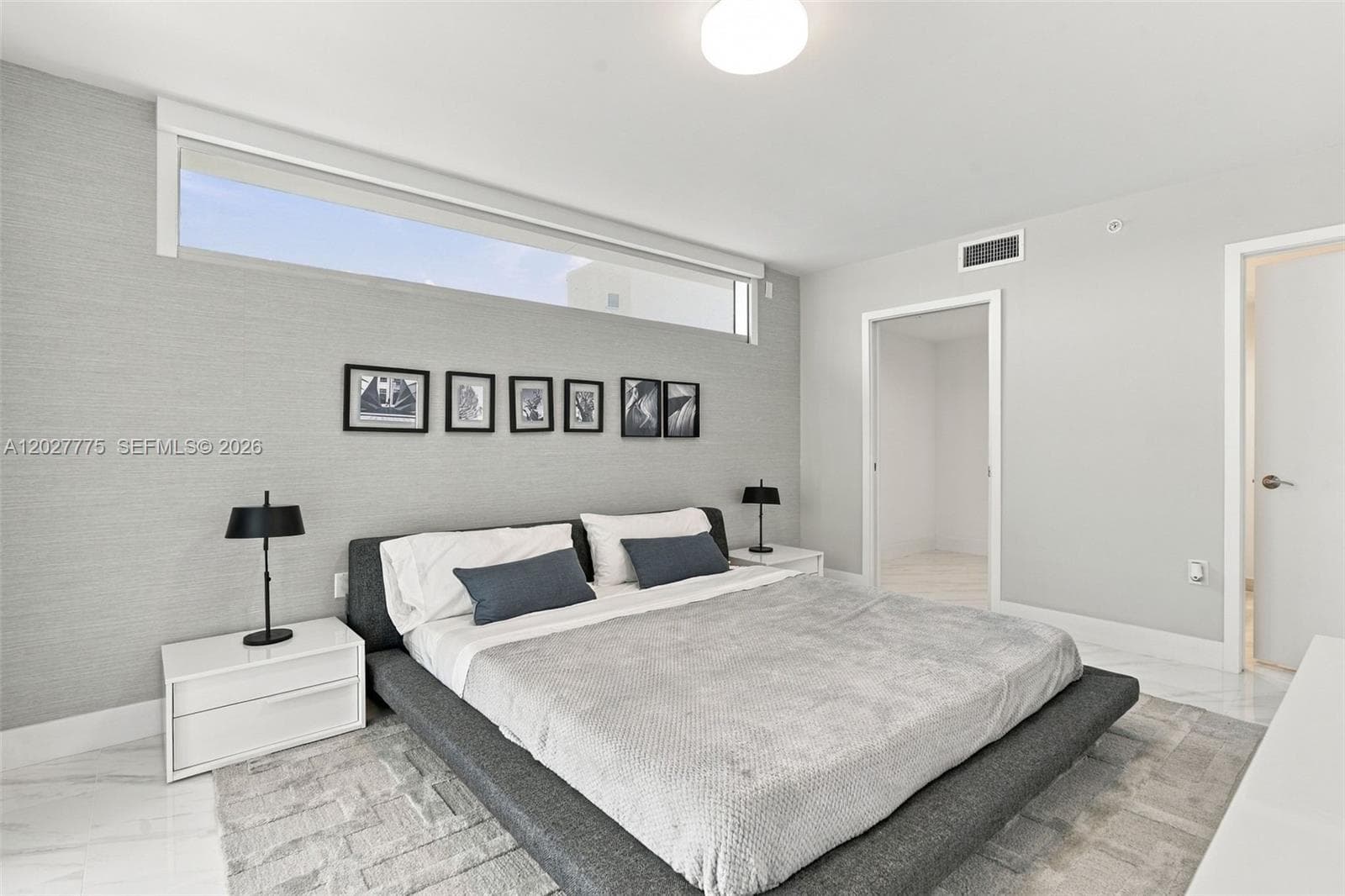 Modern ceiling light fixture, high transom window, light-toned wall covering, white flat panel door, and polished tile flooring