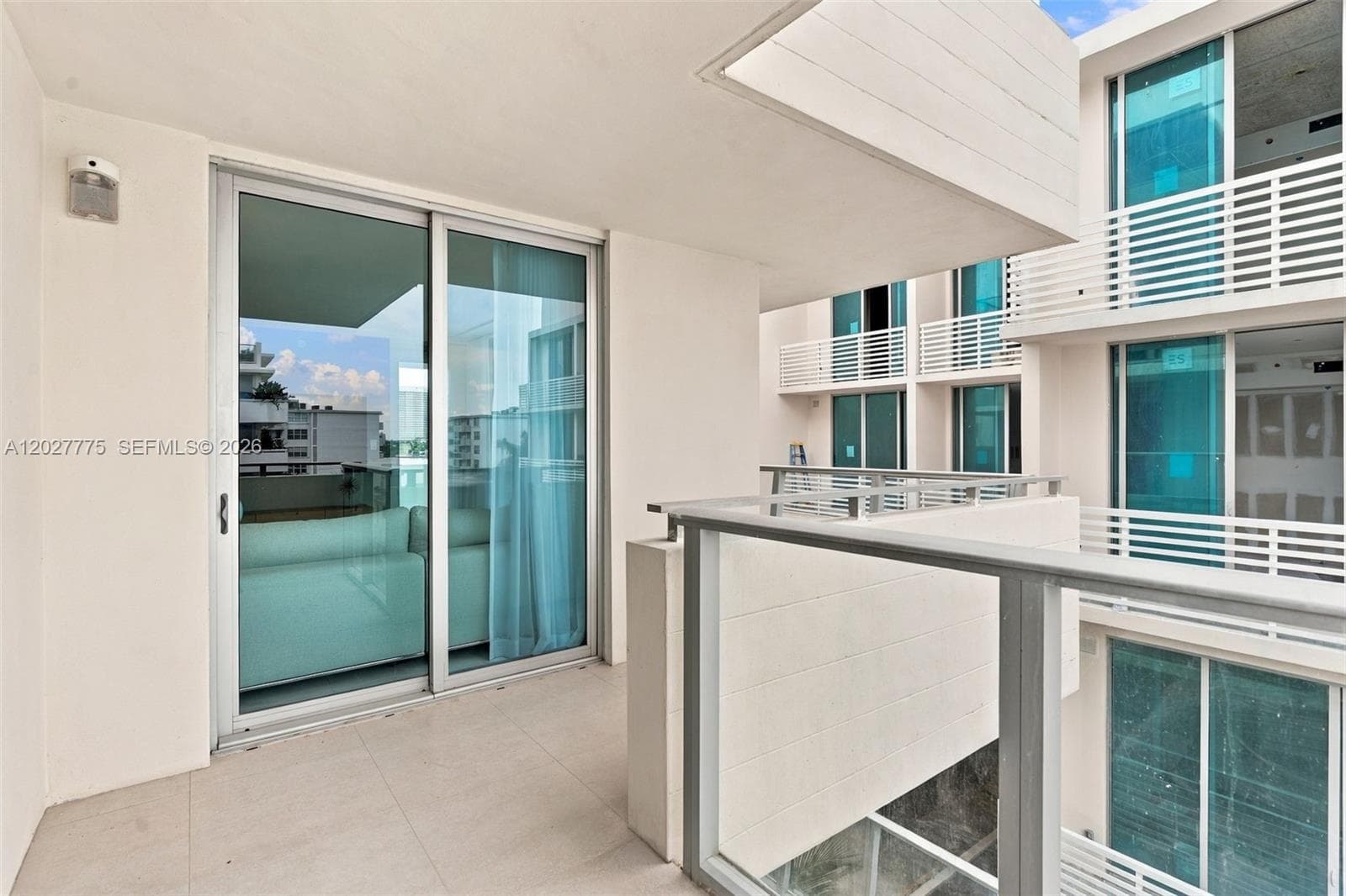 Balcony with tile flooring, aluminum-framed sliding glass doors, glass and metal railing, and an exterior wall light fixture