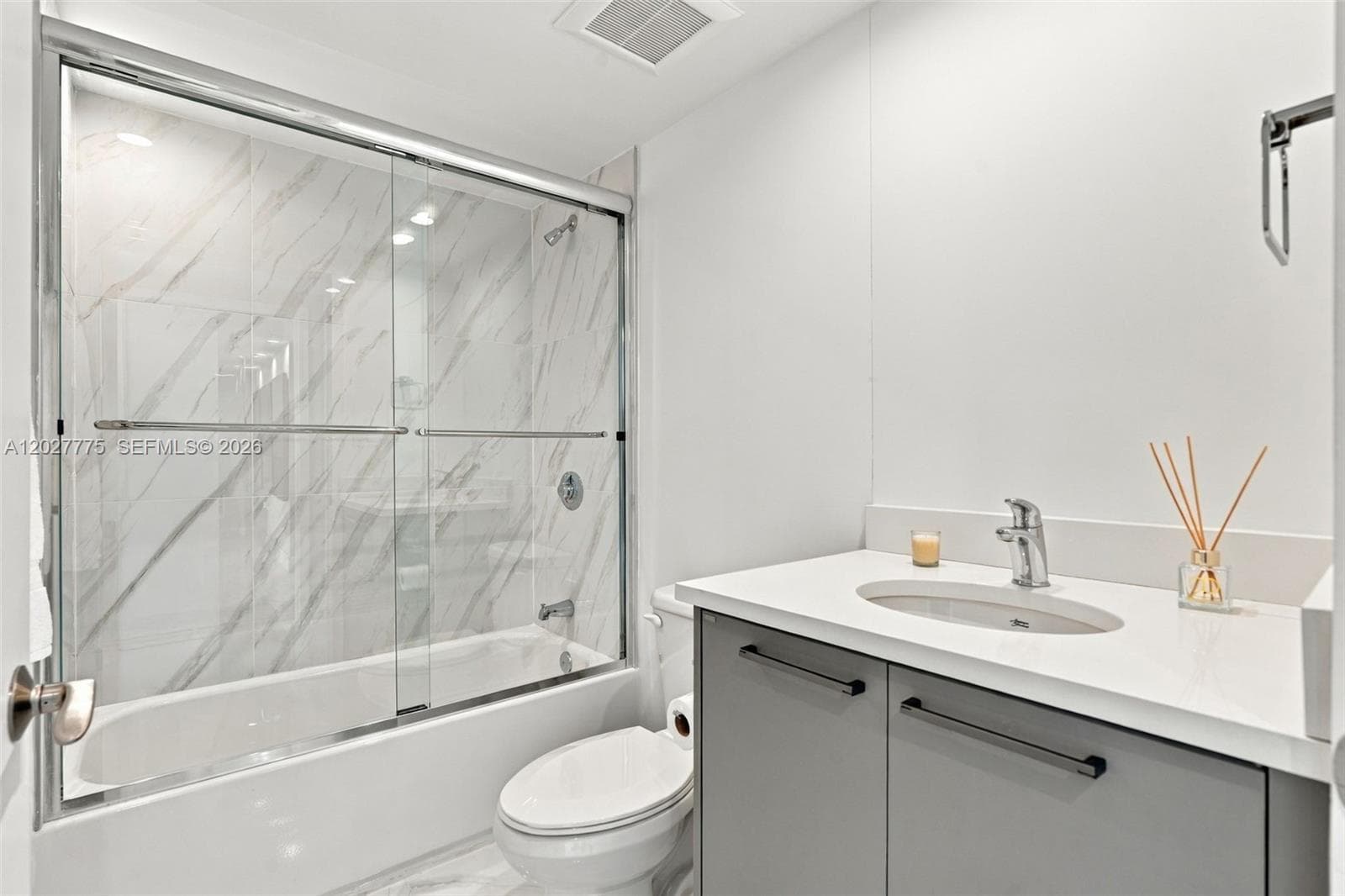 Bathtub with clear sliding glass shower doors and marble-patterned tile surround