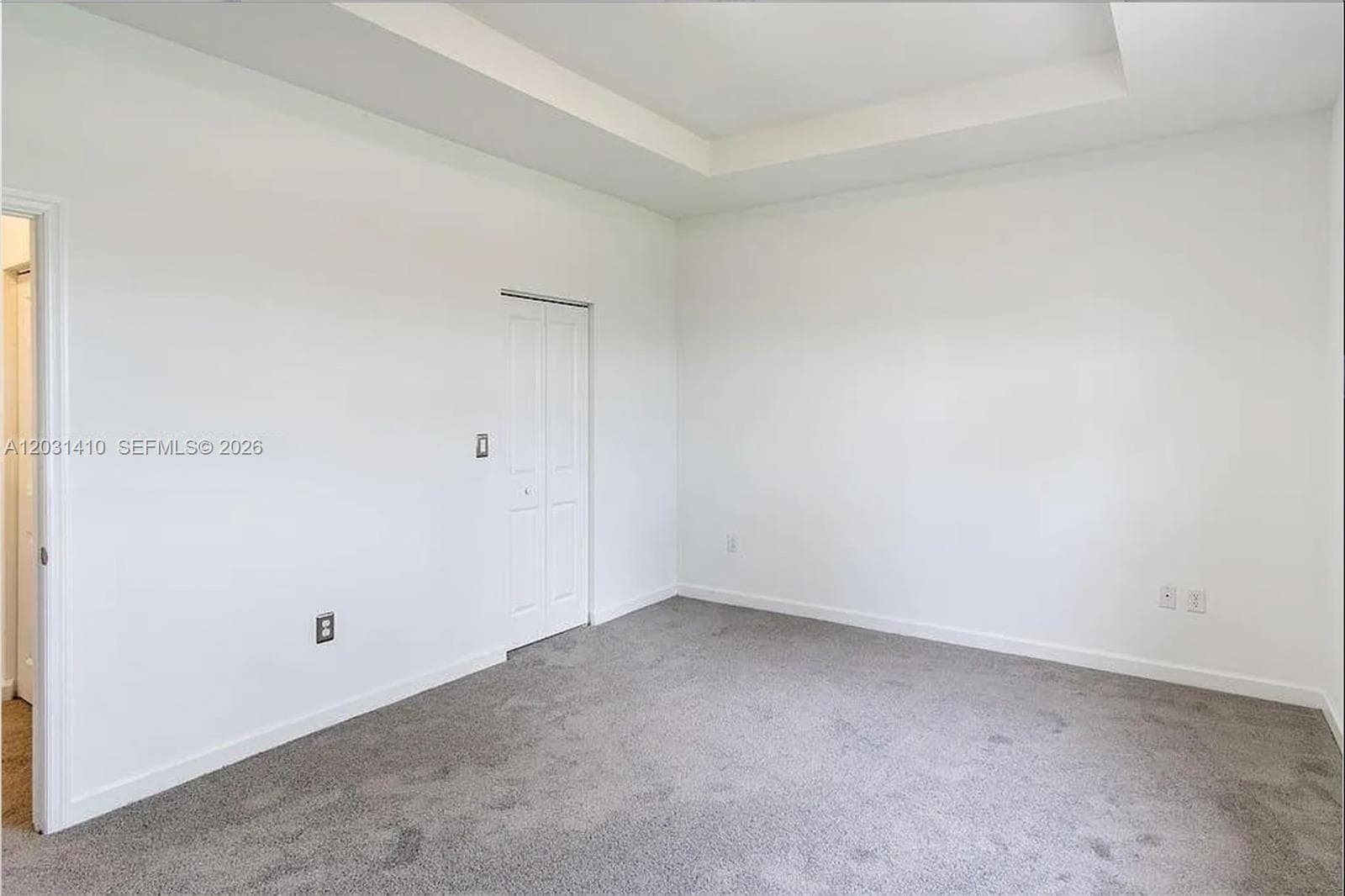 Neutral-toned interior space featuring a recessed tray ceiling, wall-to-wall carpeting, and a bifold closet door