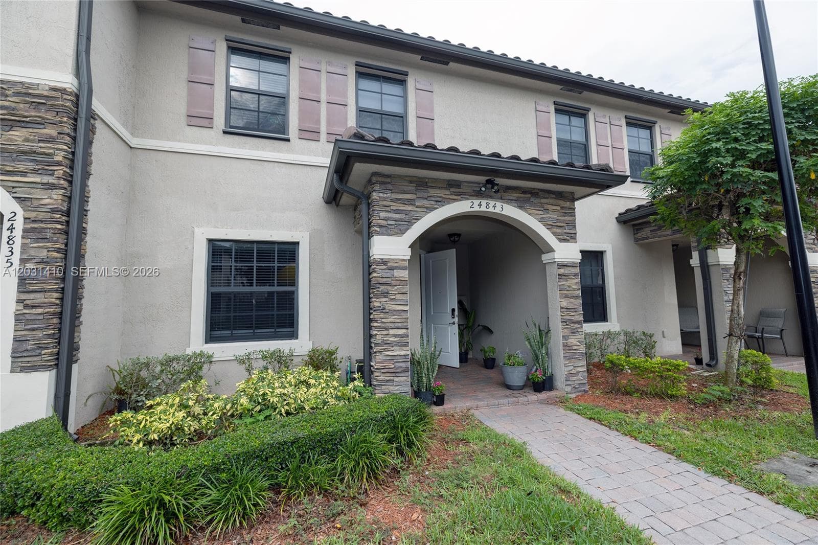 Stucco exterior featuring stacked stone accents, decorative window shutters, a covered arched entryway, and a paved walkway