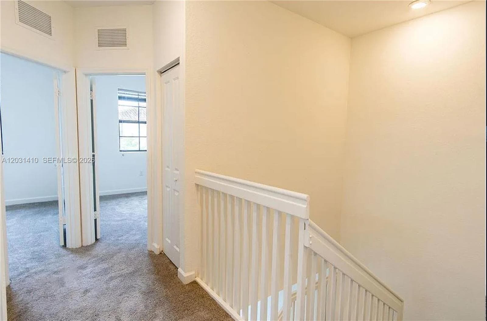 Hallway featuring grey carpeting, white bifold closet doors, and white railing