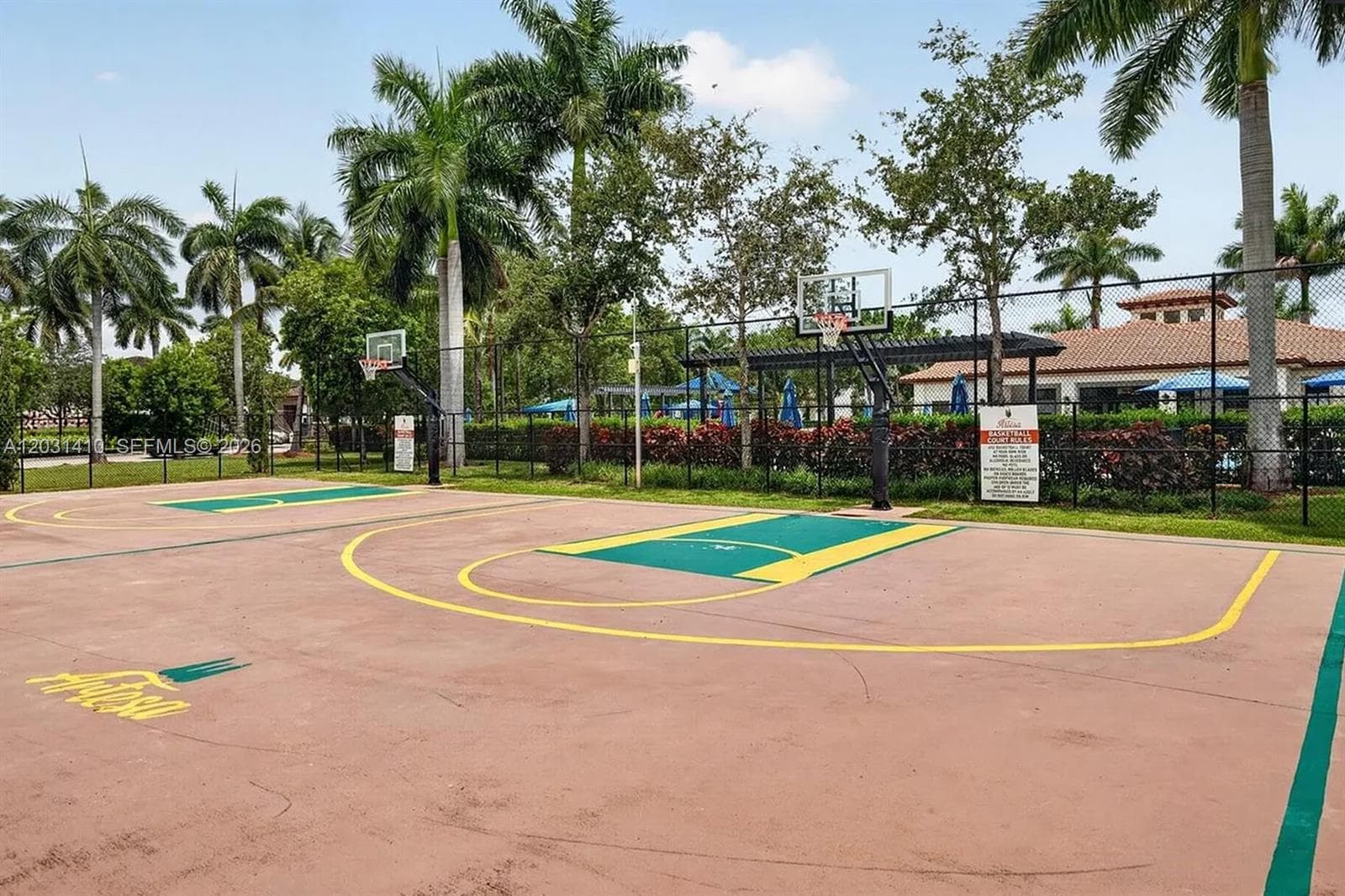 Outdoor basketball court with a multi-surface finish, perimeter fencing, and mature landscaping
