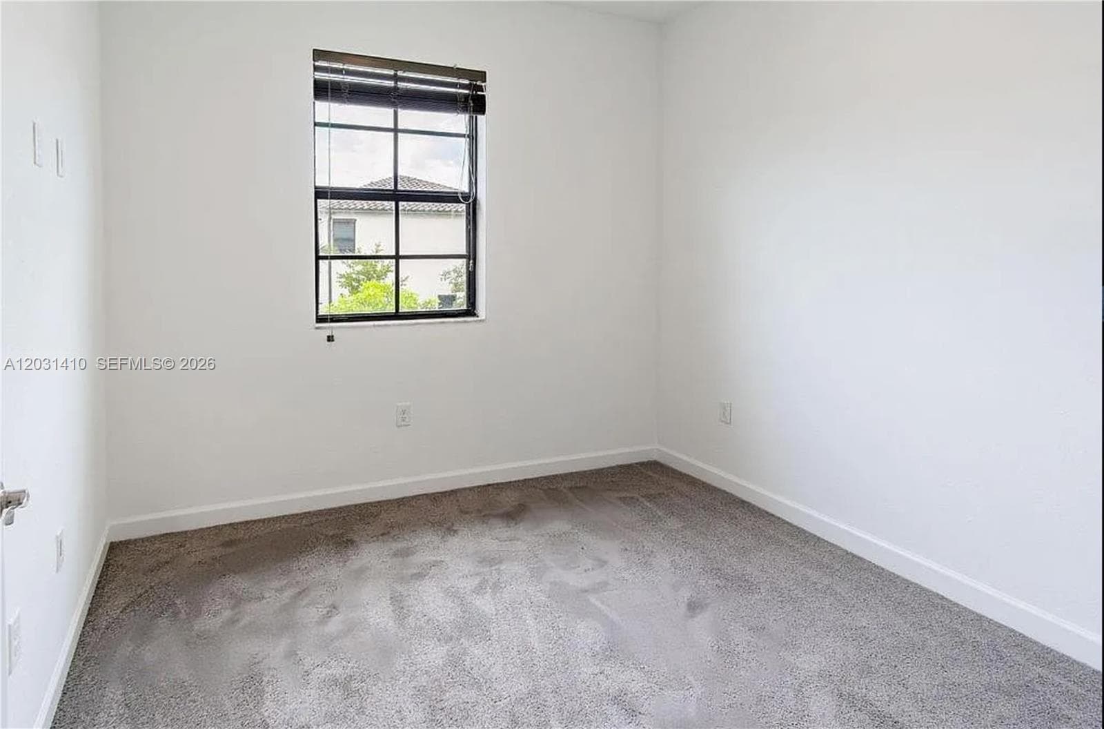 Neutral-toned interior space featuring plush carpeting and a grid-patterned window with black framing