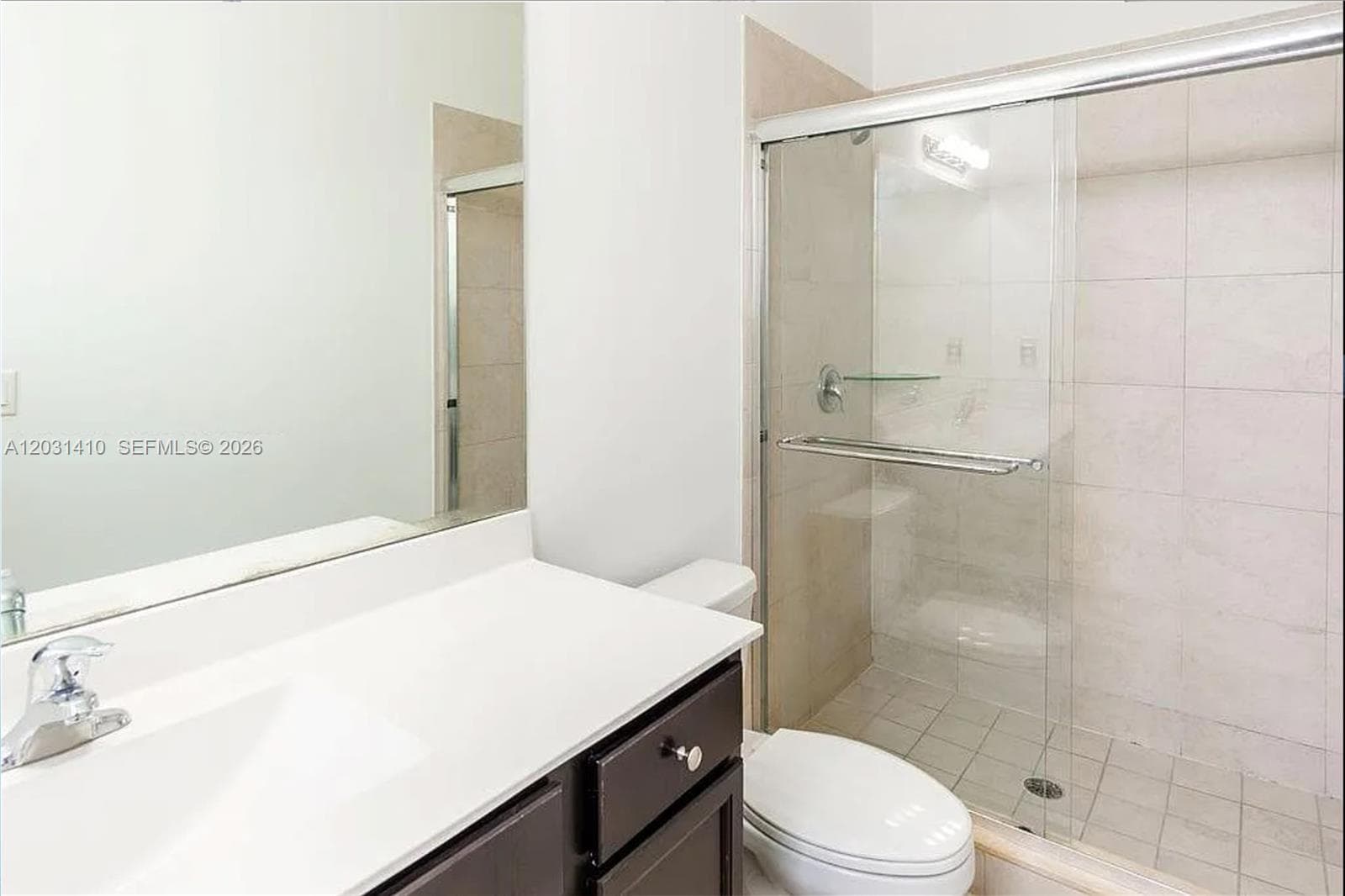 Bathroom vanity featuring a solid surface countertop, integrated sink, dark-finish cabinetry, and a large-format mirror paired with a walk-in shower enclosure featuring floor-to-ceiling tile surround and glass sliding doors
