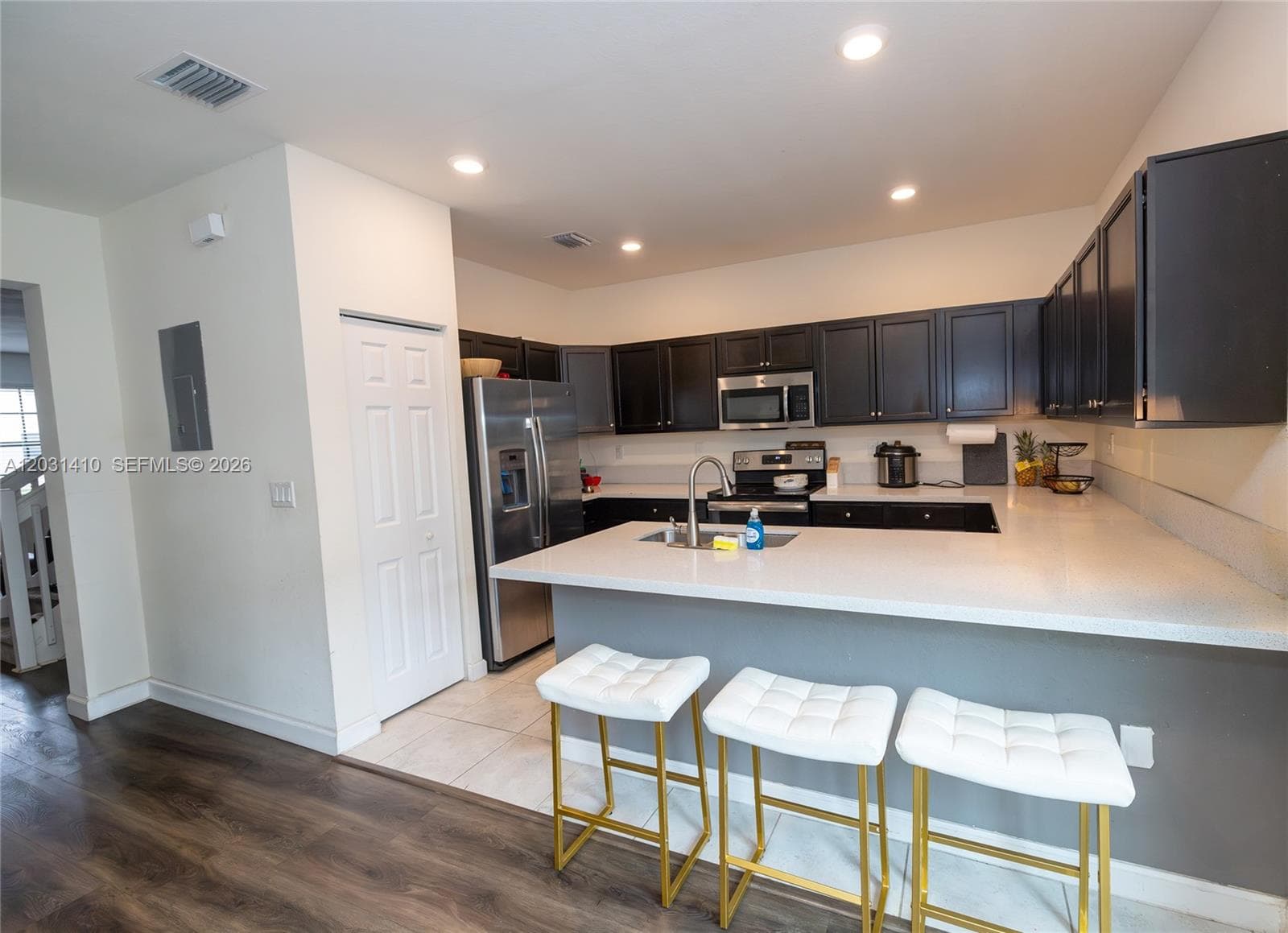 Kitchen featuring dark cabinetry, expansive countertop, stainless steel refrigerator, built-in microwave, and wood-finish flooring