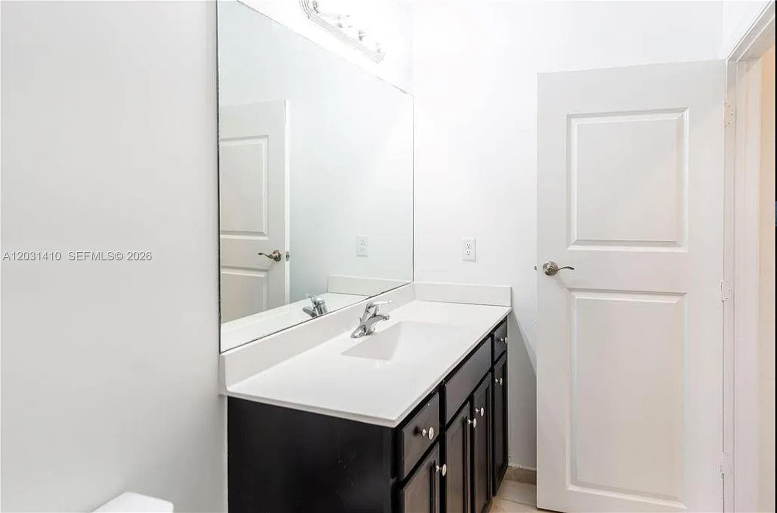 Dark-finished cabinetry featuring a white countertop with an integrated sink, a large wall-mounted mirror, and a multi-paneled interior door