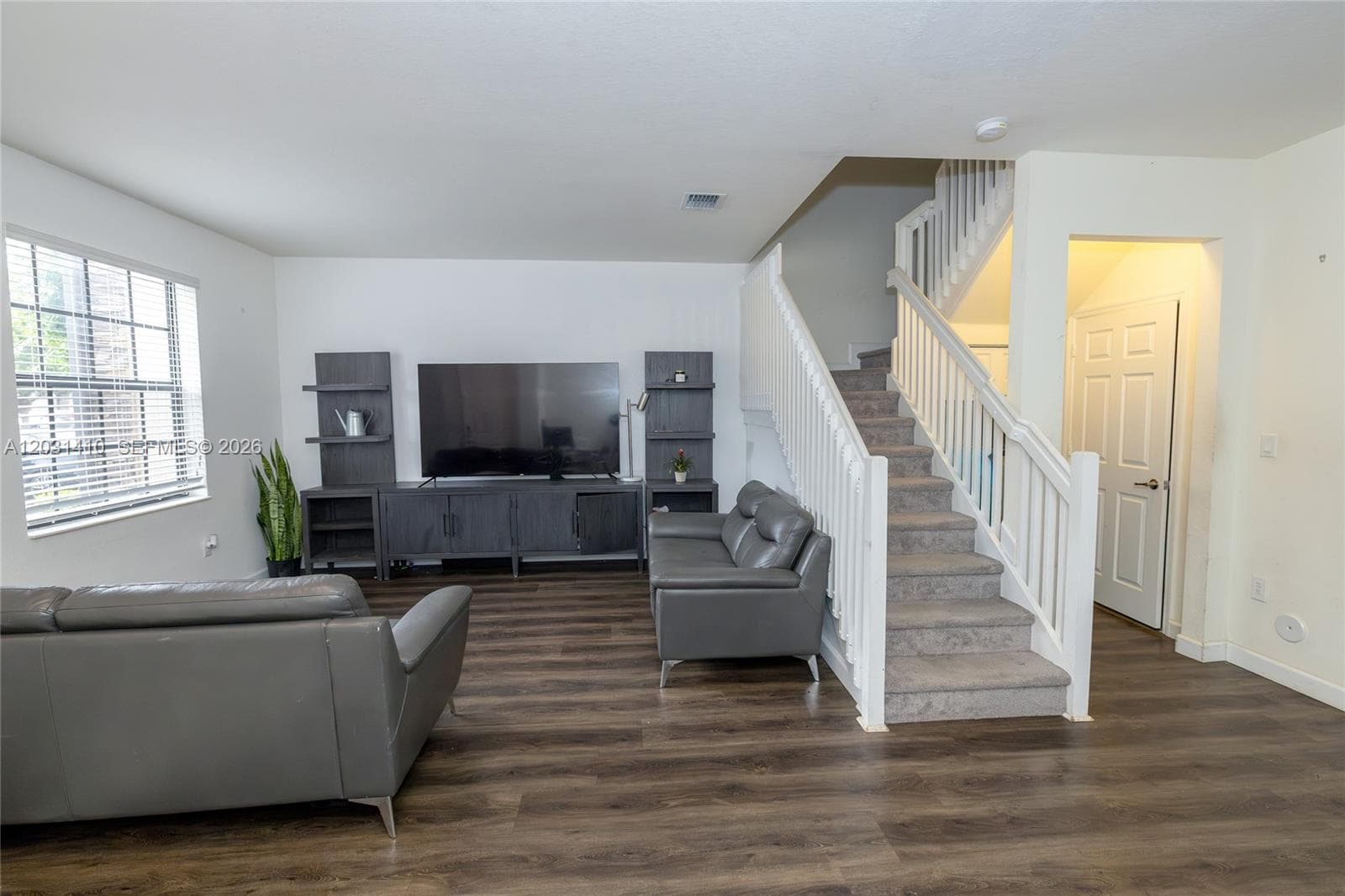 Living area featuring wood-finish flooring, built-in media shelving, staircase with white railing, and multi-pane window