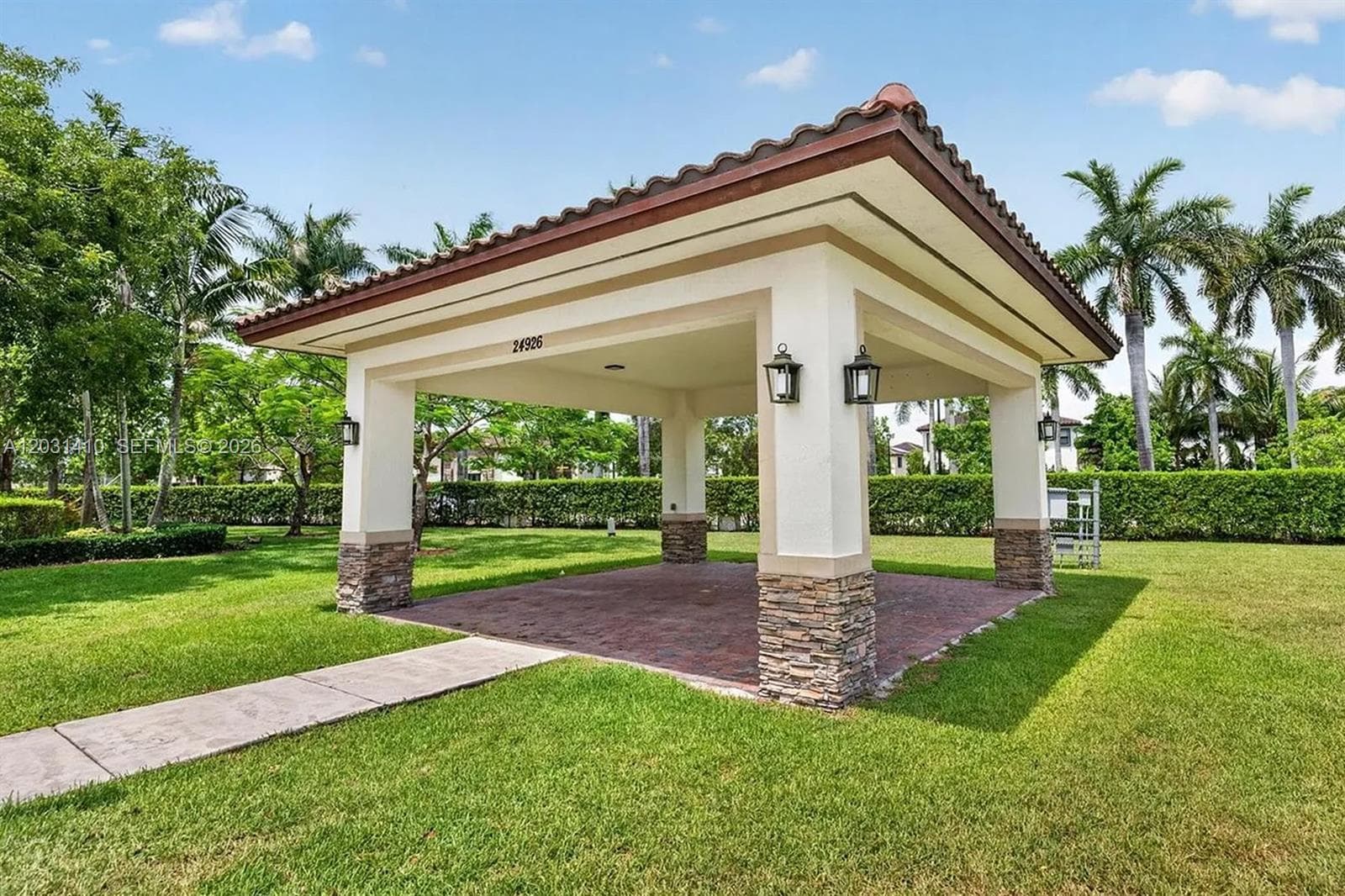 Outdoor pavilion featuring a tile roof, stone-accented support columns, brick-paved flooring, and wall-mounted exterior lighting