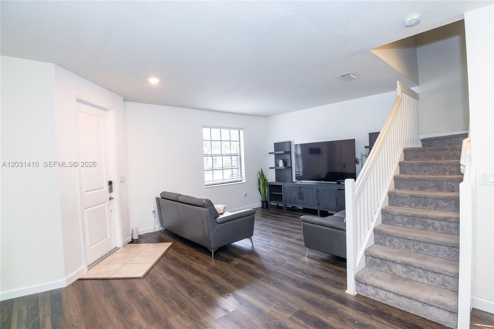 Wood-finish flooring, staircase with a white balustrade and carpeted treads, ceramic tile entryway, and neutral wall tones