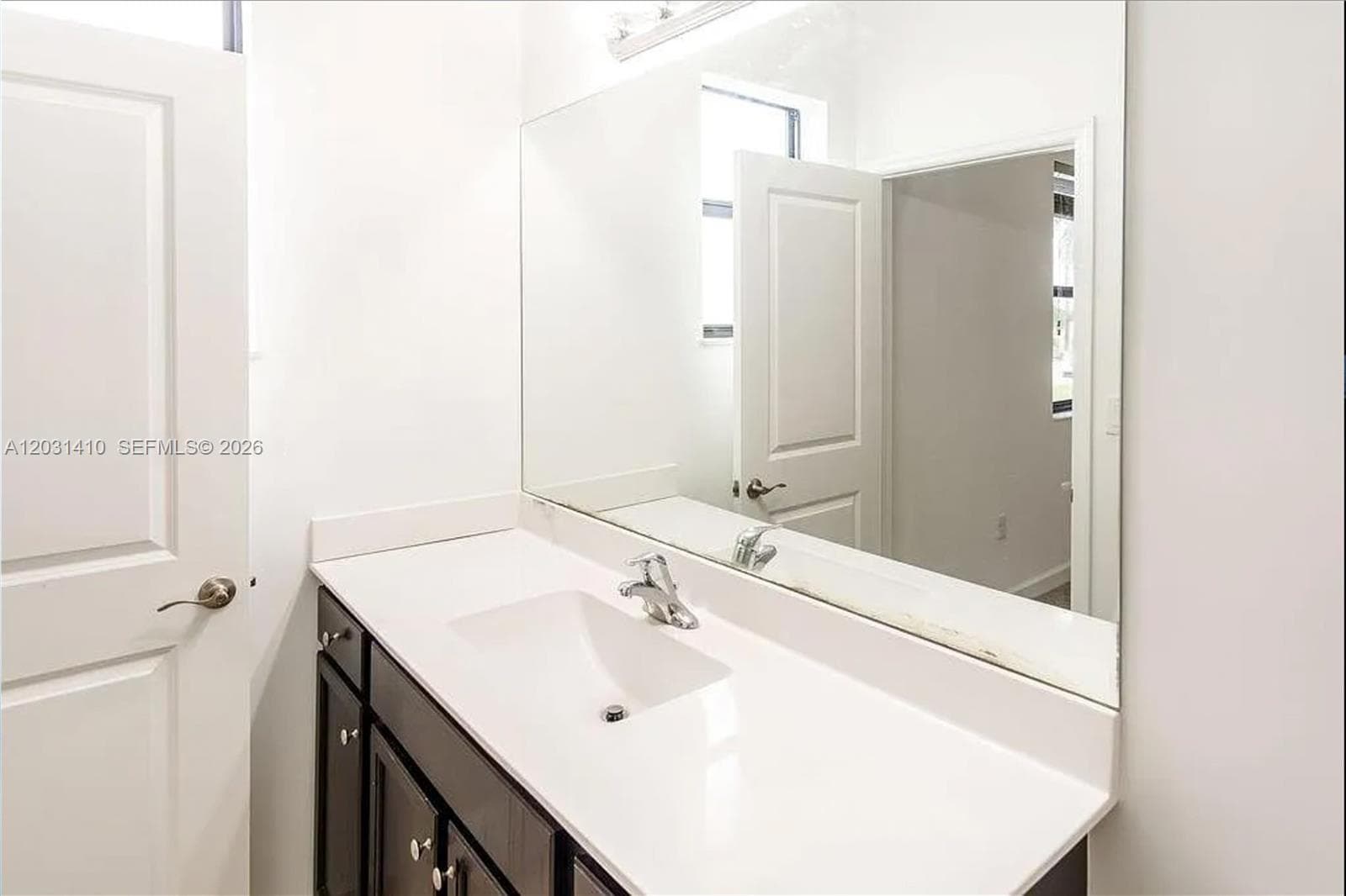 Bathroom vanity featuring a dark-finish wood cabinet, a white solid-surface countertop with an integrated sink, a full-width wall mirror, and a multi-bulb vanity light fixture
