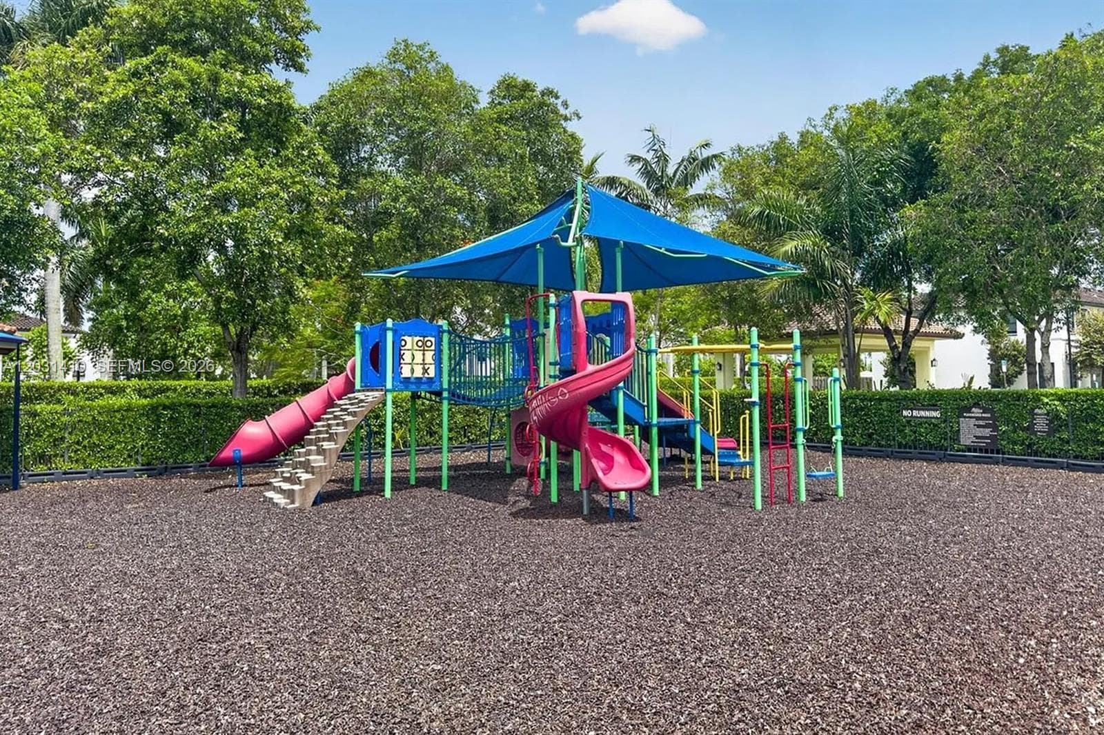Community playground featuring a multi-level structure with spiral and straight slides, a protective canopy, climbing elements, and a ground covering of wood mulch