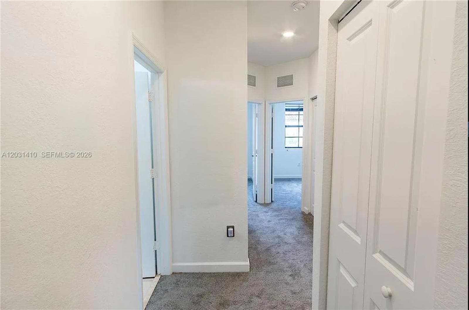 Interior hallway featuring neutral-toned carpeting, white walls, multiple interior doors, and a built-in closet with bi-fold doors