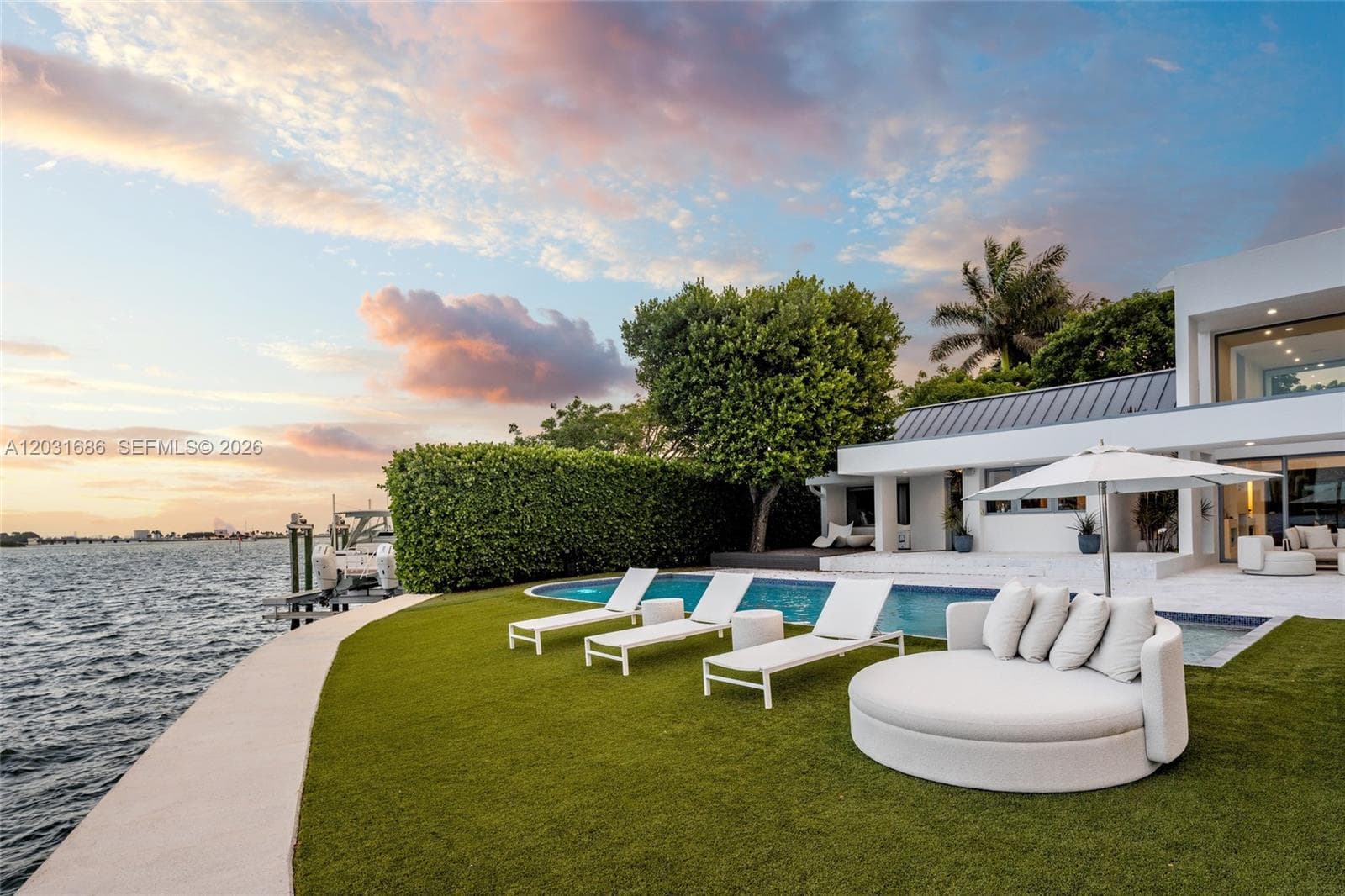 Waterfront estate featuring a curvilinear swimming pool, concrete seawall, private boat dock, synthetic lawn, and a multi-level exterior structure