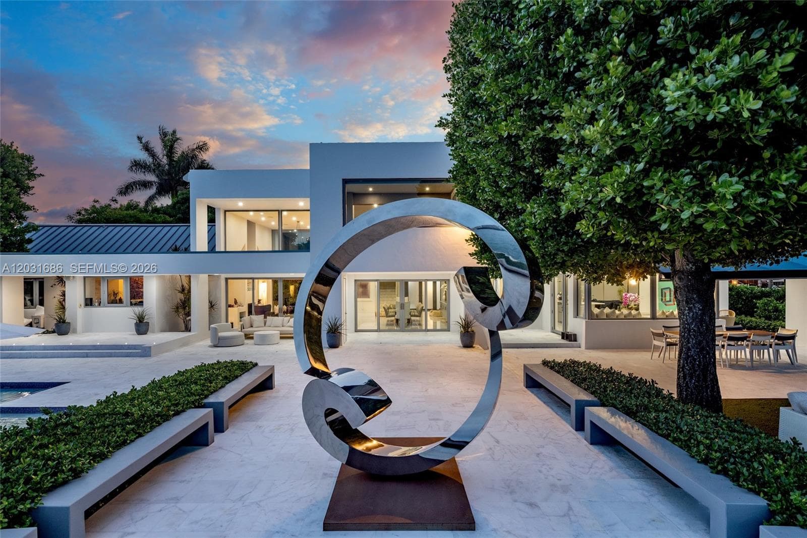 Modern architectural exterior featuring smooth stucco finishes, expansive glass sliding doors, stone-tiled patio, and integrated built-in concrete benches