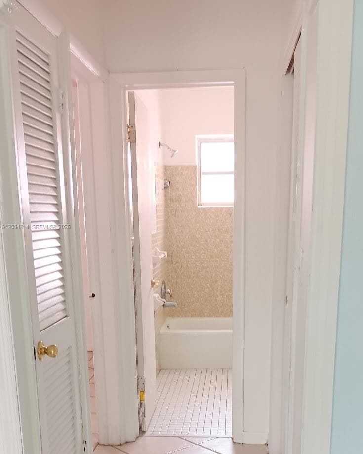 Louvered closet doors, white mosaic tile flooring, and a bathtub with textured wall tiling
