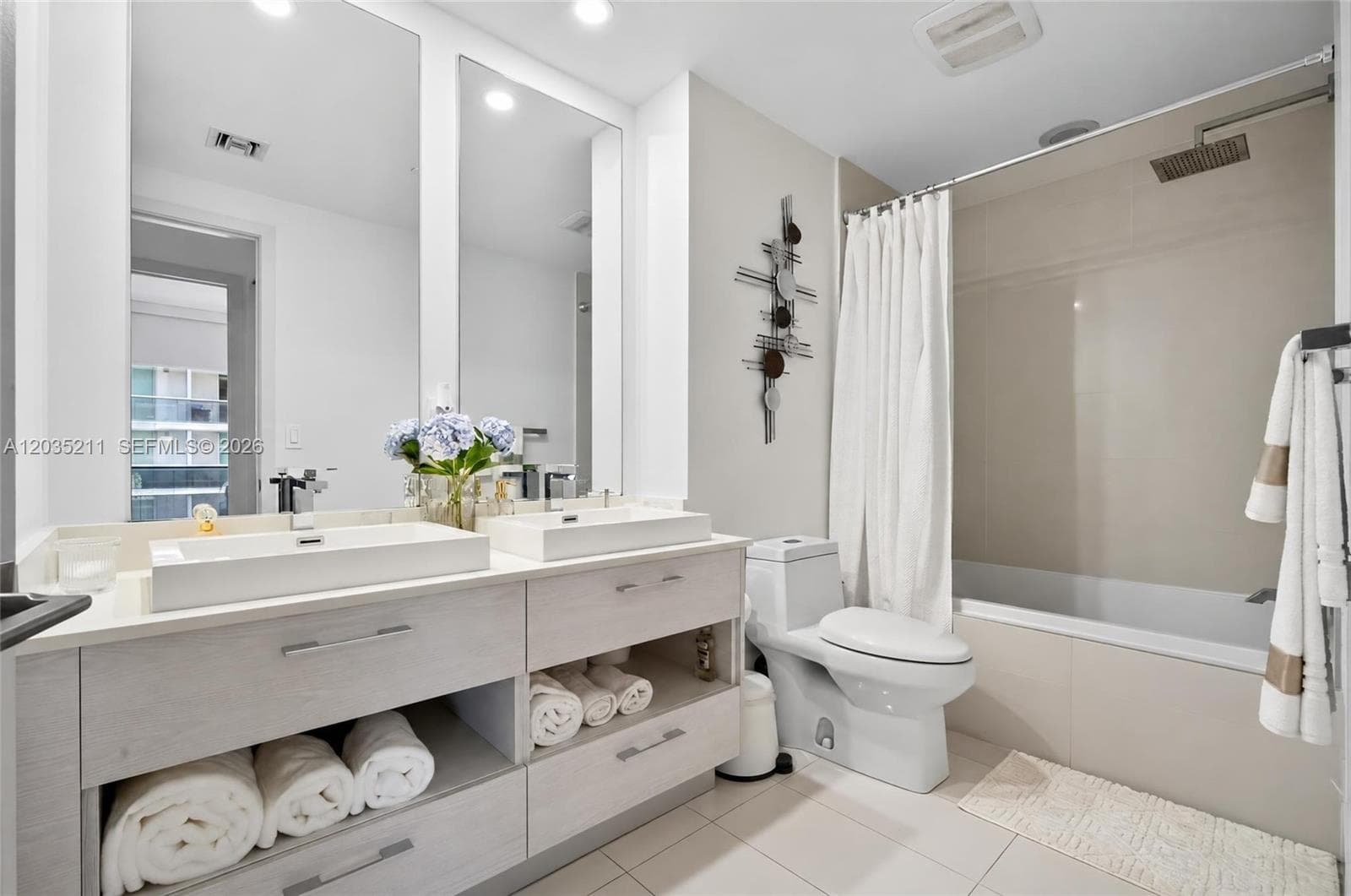 Dual-basin floating vanity with rectangular vessel sinks and stone-surface countertop, complemented by floor-to-ceiling mirrors, tile flooring, and a shower-tub combination featuring a rain-style showerhead