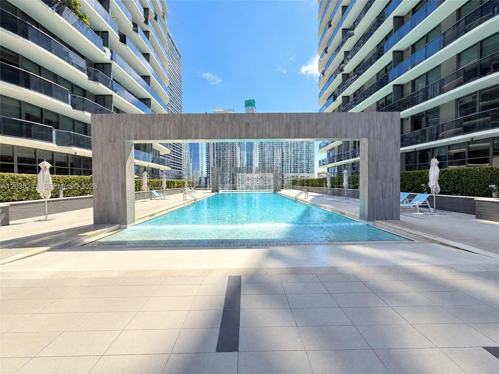 Swimming pool featuring a stone-finish archway, integrated water feature, perimeter landscaping, and tile decking