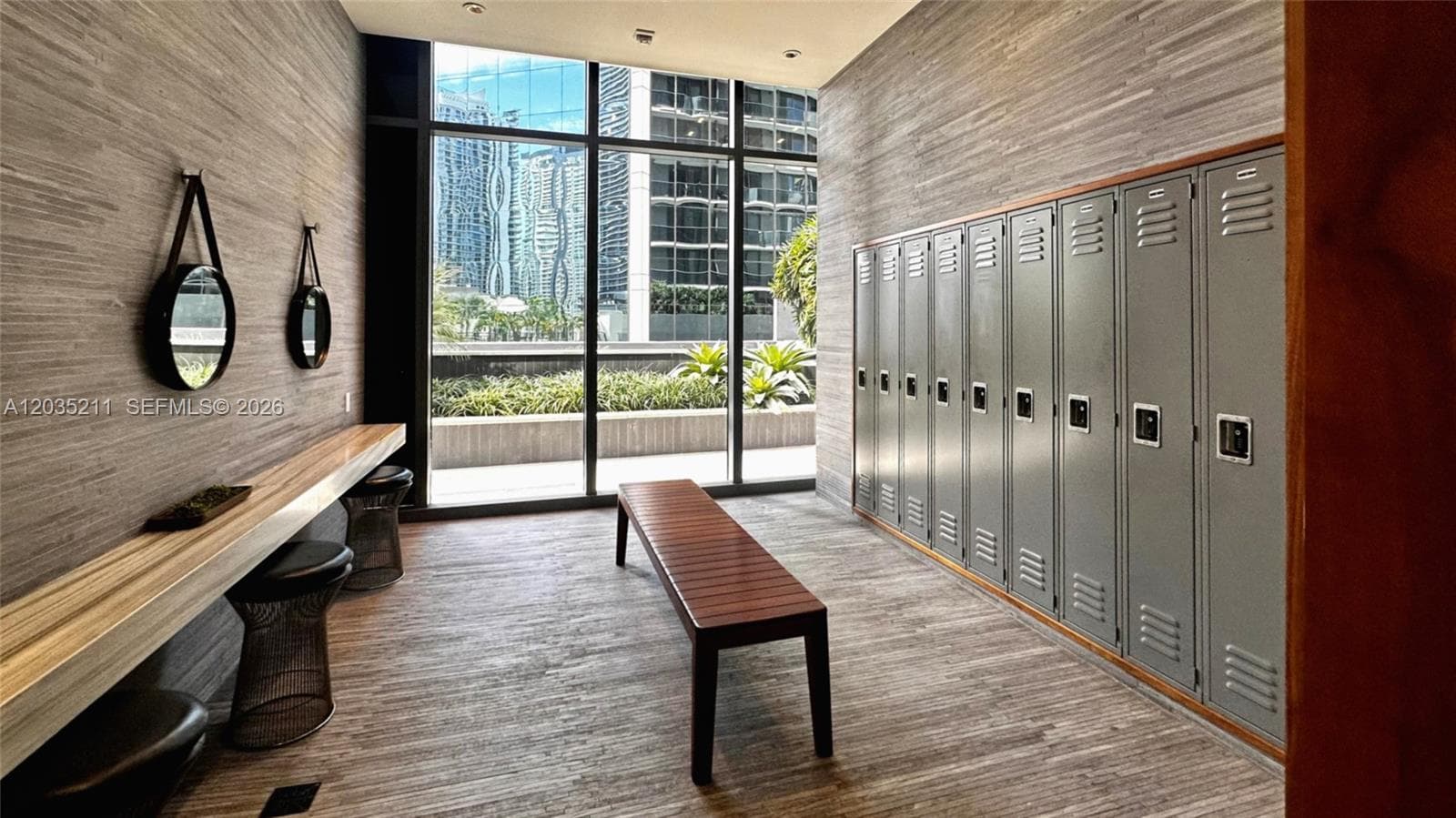 Floor-to-ceiling windows, wall-to-wall metal lockers, wood-textured wall cladding, recessed lighting, and a floating wood counter