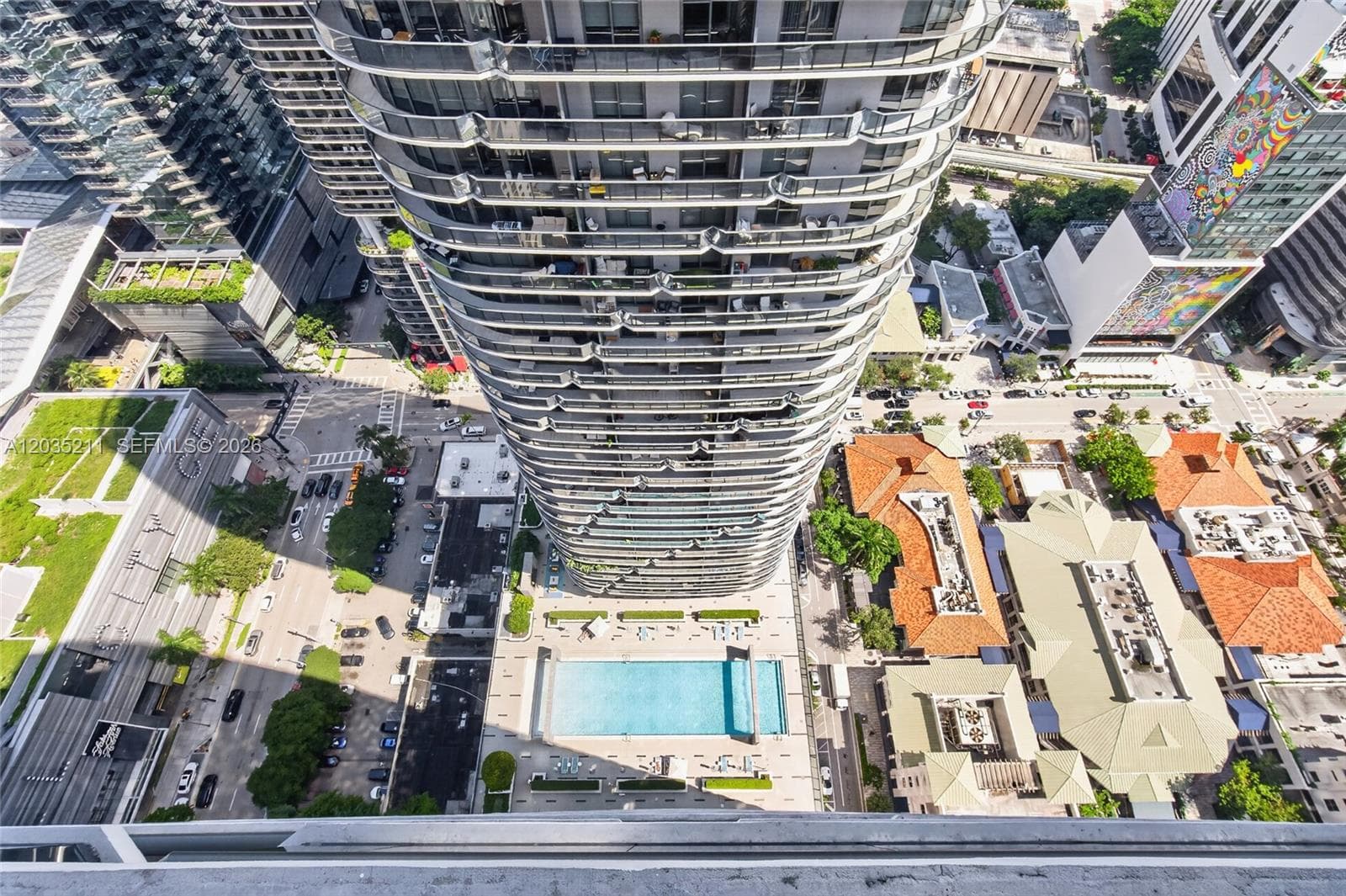High-rise tower featuring wrap-around glass balconies, an outdoor ground-level swimming pool, and paved deck hardscaping