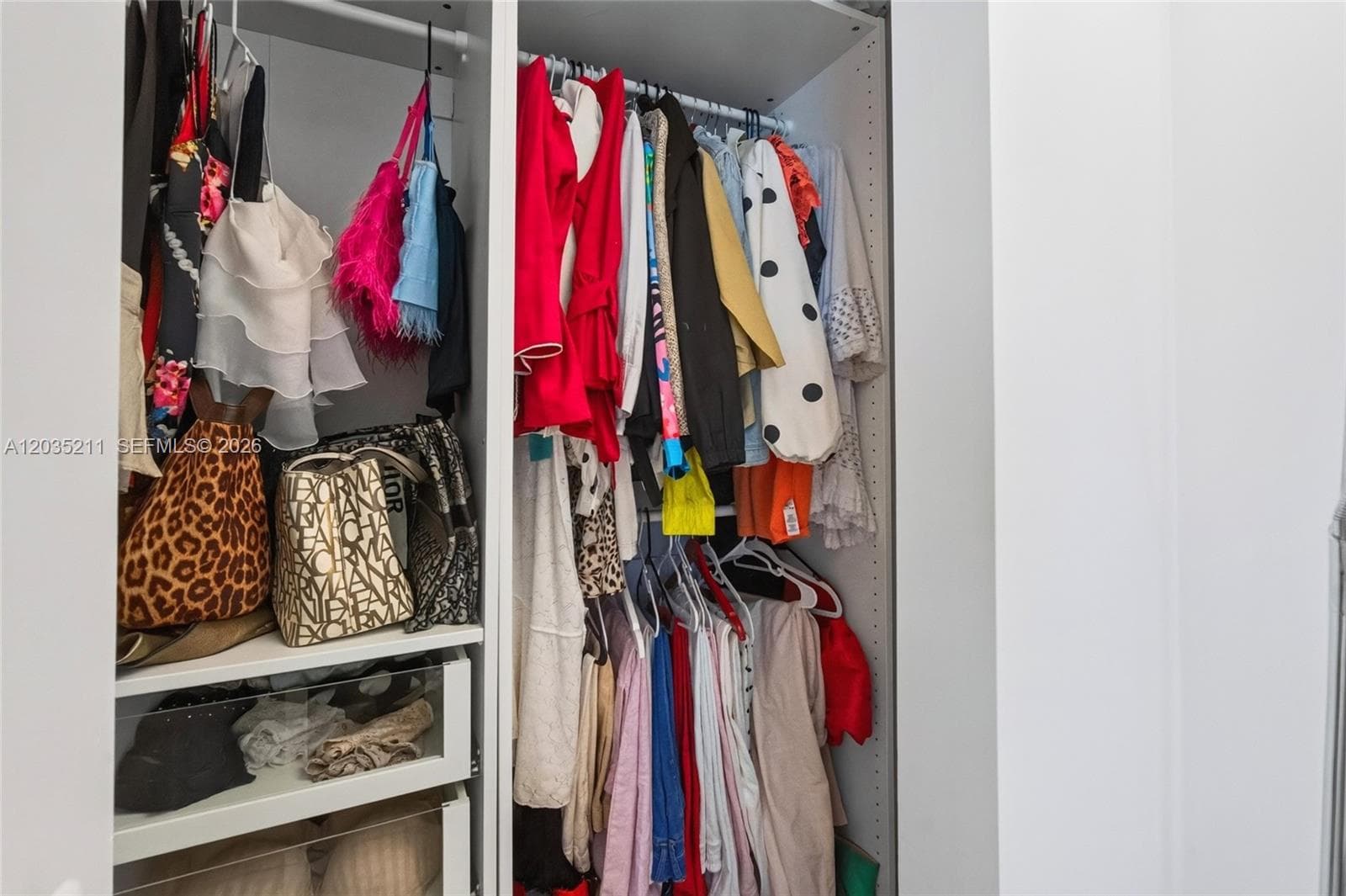 Custom reach-in closet featuring white modular shelving, multiple hanging rods, and integrated pull-out drawers with glass-panel fronts