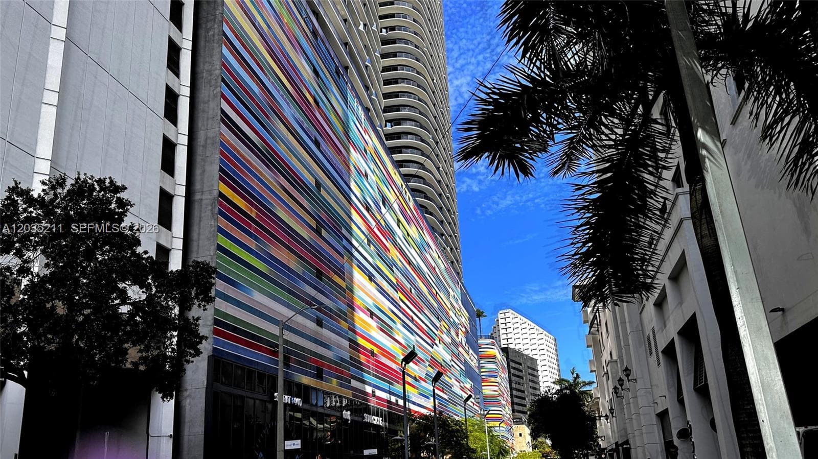 High-rise building exterior featuring a multi-colored, linear facade design, sleek glass balcony railings, and a prominent concrete structure