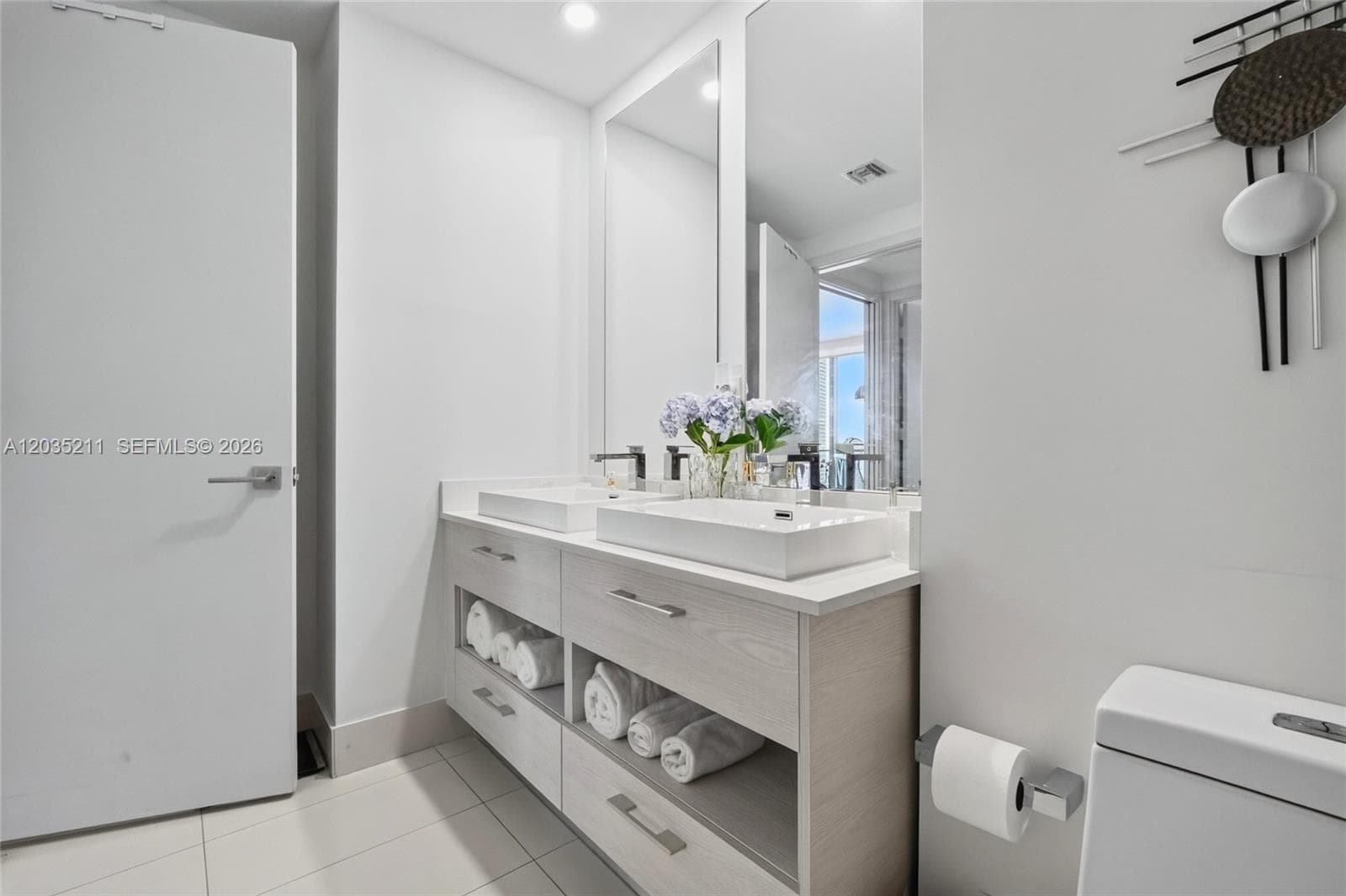 Dual-sink floating vanity with wood-finish cabinetry, rectangular vessel sinks, expansive wall-mounted mirror, and polished metal hardware