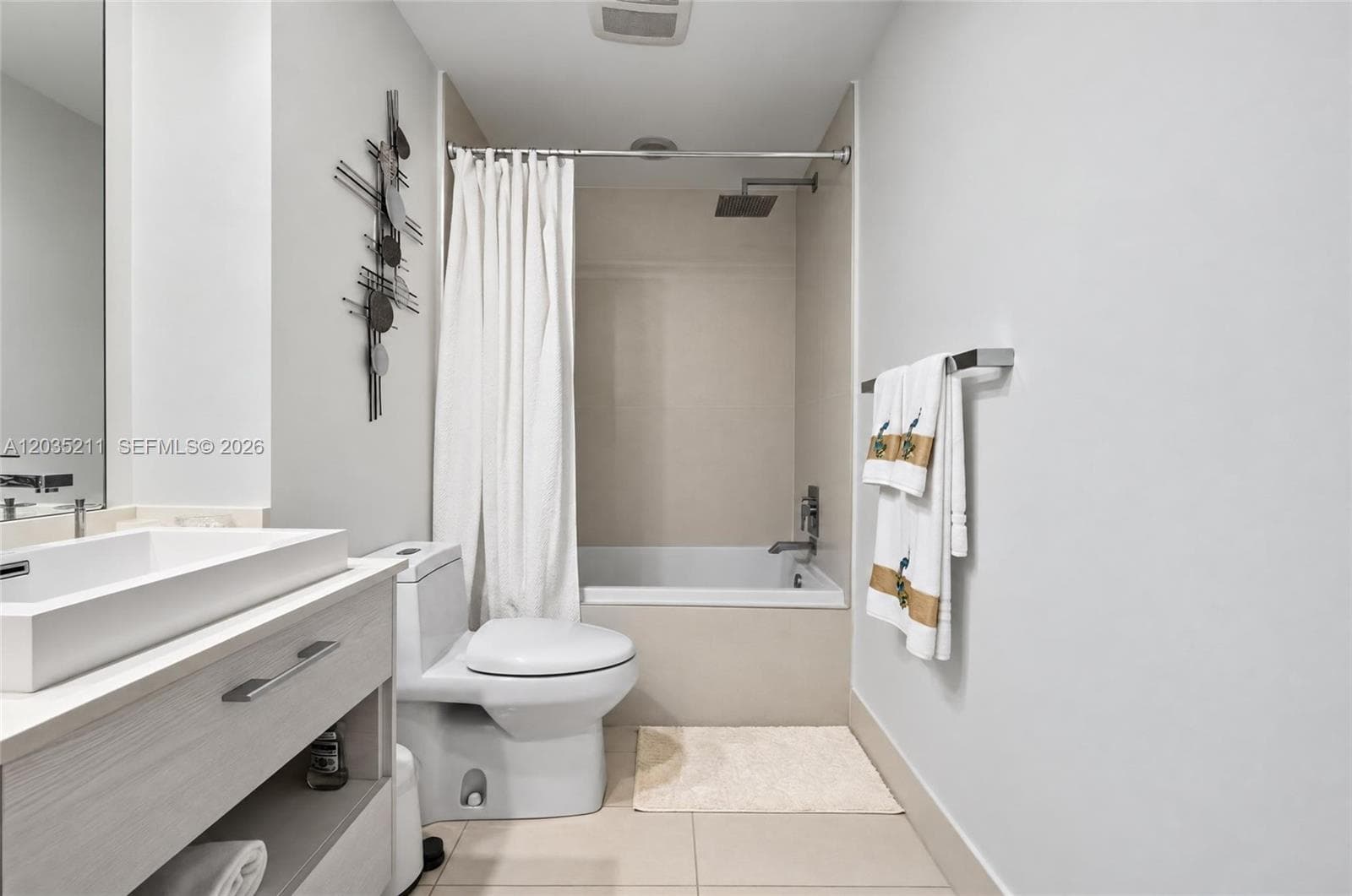 Floating vanity with a rectangular vessel sink, wall-mounted faucet, square-profile tub with a rain-style showerhead, and tile flooring