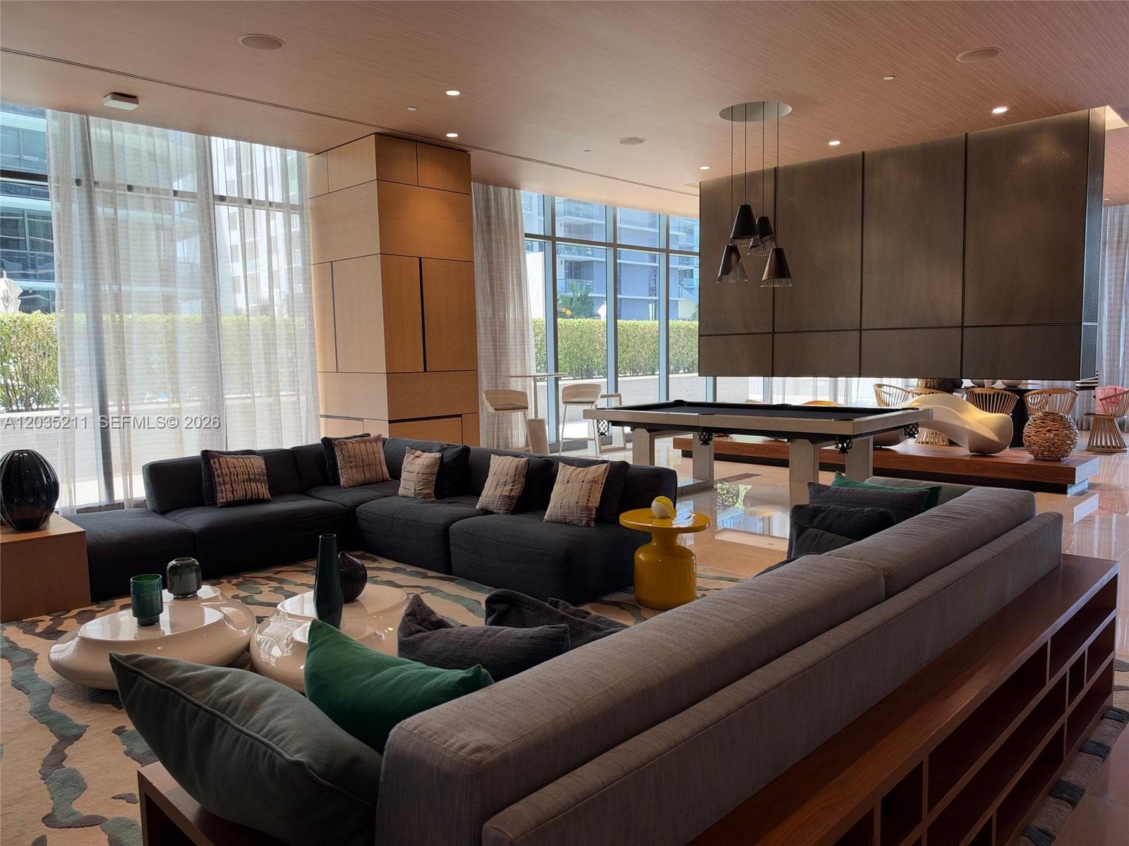 Expansive interior space featuring floor-to-ceiling windows, natural wood-finish ceiling paneling, and a large-scale metal feature wall with integrated lighting