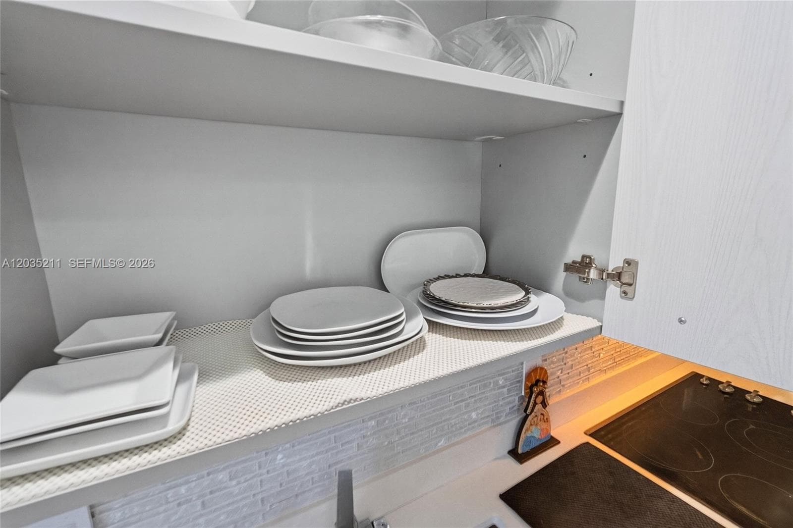 Cabinetry with a light wood-grain finish, integrated under-cabinet lighting, and textured tile backsplash