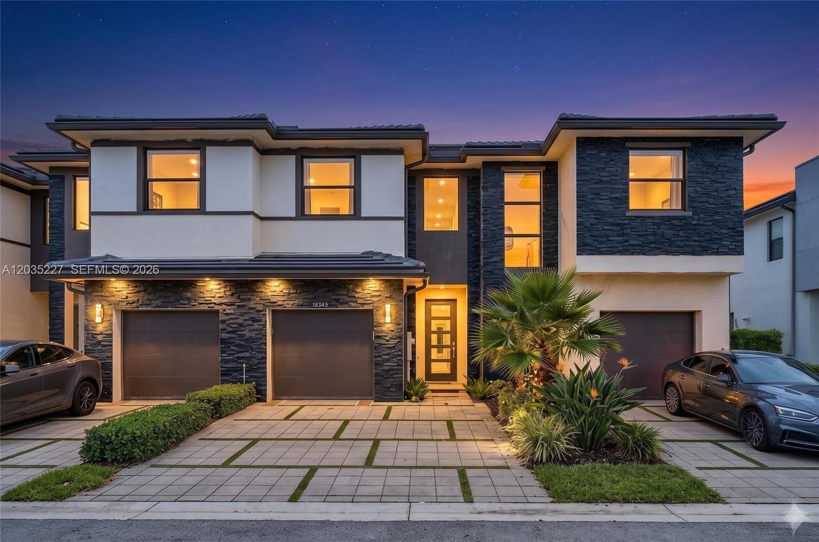 Striking twilight curb appeal showcasing a modern contemporary façade with sleek stacked-stone accents and warm architectural lighting. Tropical landscaping and a paver driveway frame the dramatic entrance, all set against a vivid sunset sky.