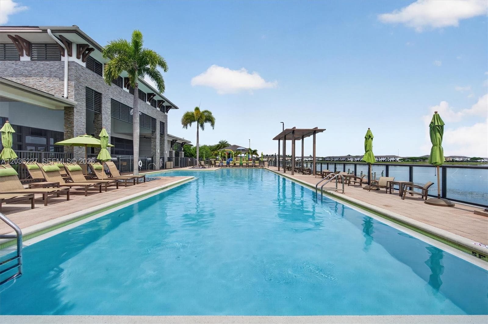 Family-friendly kids' splash pool featuring a colorful slide and water play structure, set against scenic lake views. Shaded loungers and a covered gazebo provide the perfect spot for parents to relax nearby.