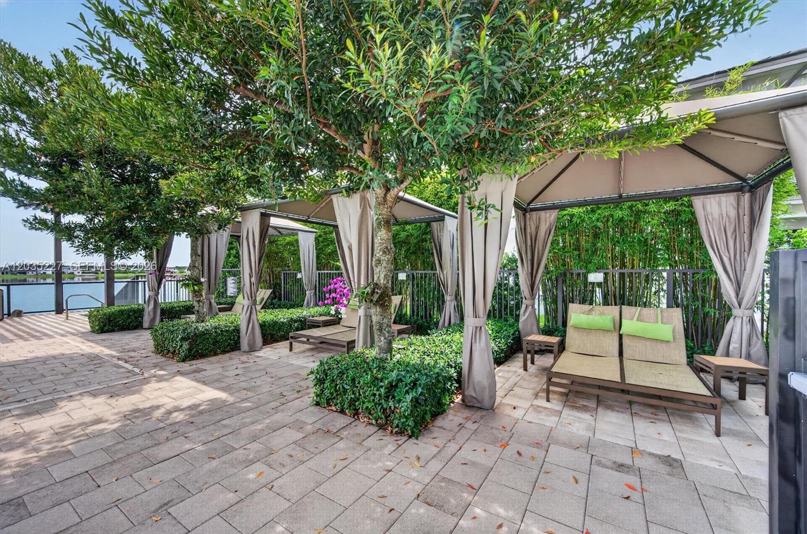 Resort-style cabana lounge area shaded by mature trees and lush bamboo landscaping, offering a tranquil waterfront retreat. Curtained cabanas with plush loungers create a private oasis for residents to unwind.