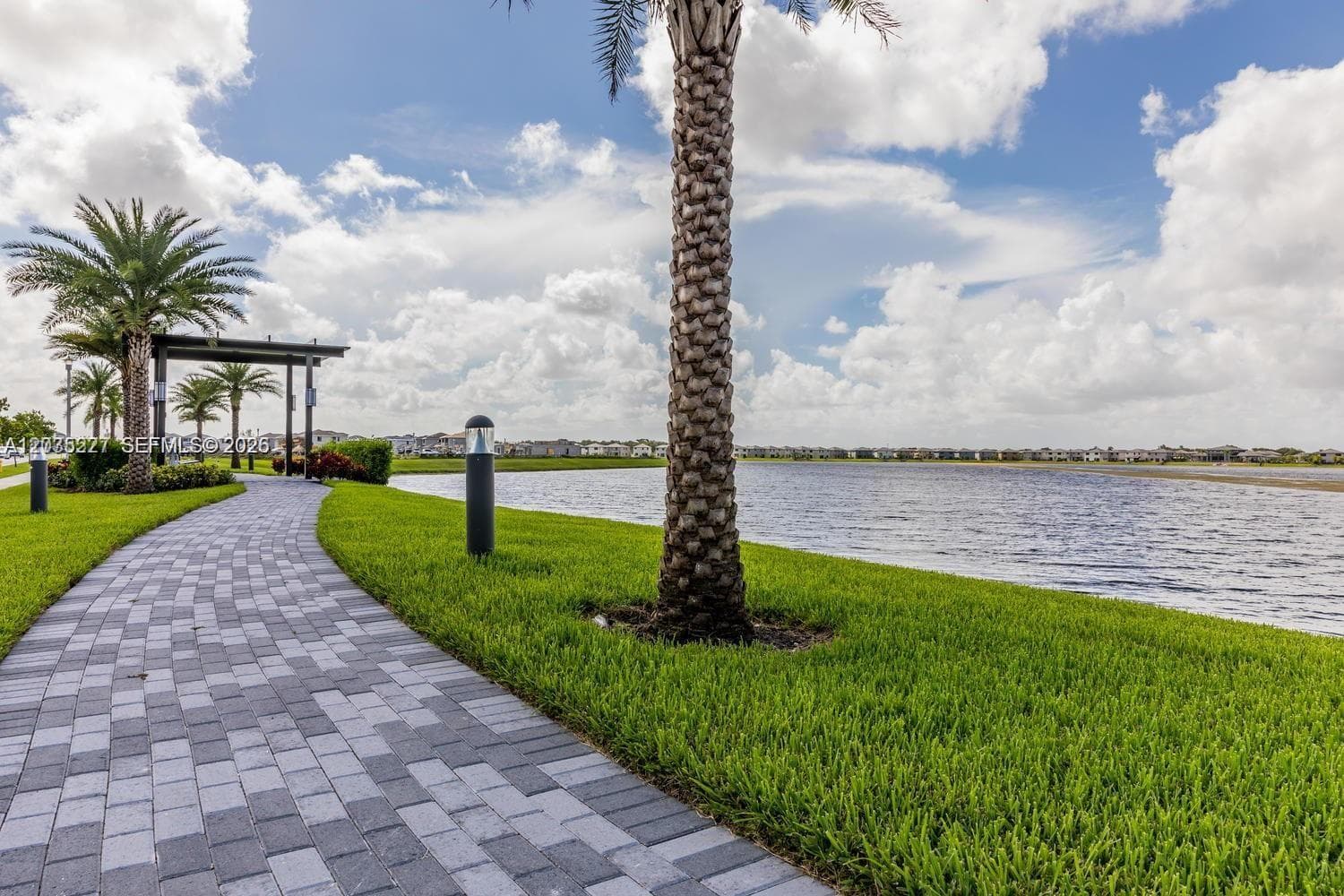 Picturesque lakeside walking path lined with mature palm trees and manicured landscaping, perfect for evening strolls. Sweeping water views and a charming pergola entrance add to the community's resort-style appeal.