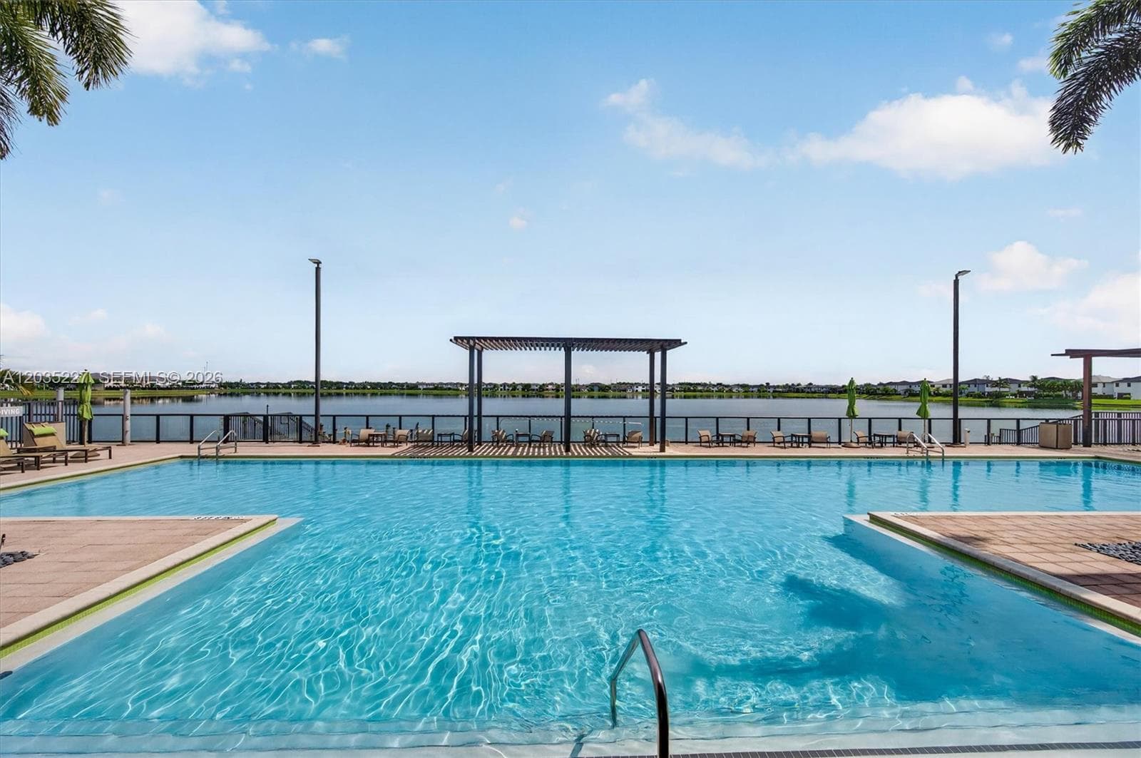 Charming community dock extending out over the sparkling lake, framed by rope railings under a wide-open sky. A peaceful waterfront escape offering panoramic views of the surrounding neighborhood.