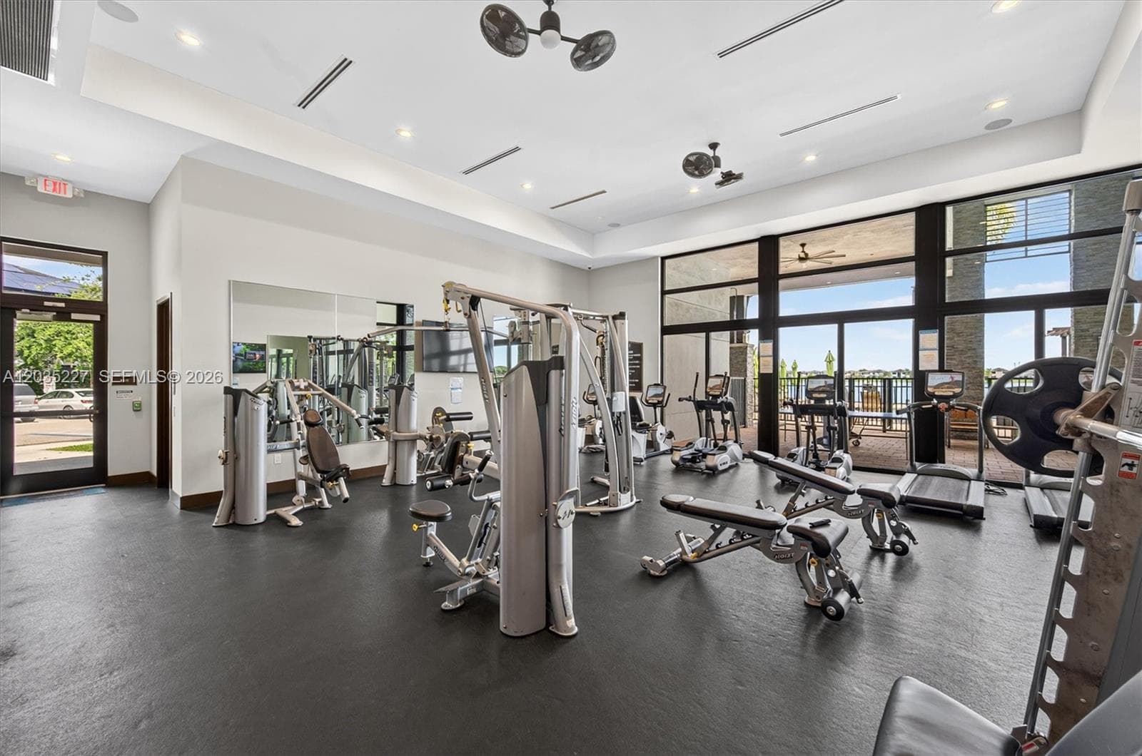 State-of-the-art fitness center equipped with premium strength and cardio machines for a complete workout. Floor-to-ceiling windows flood the space with natural light and offer scenic views of the outdoor terrace beyond.
