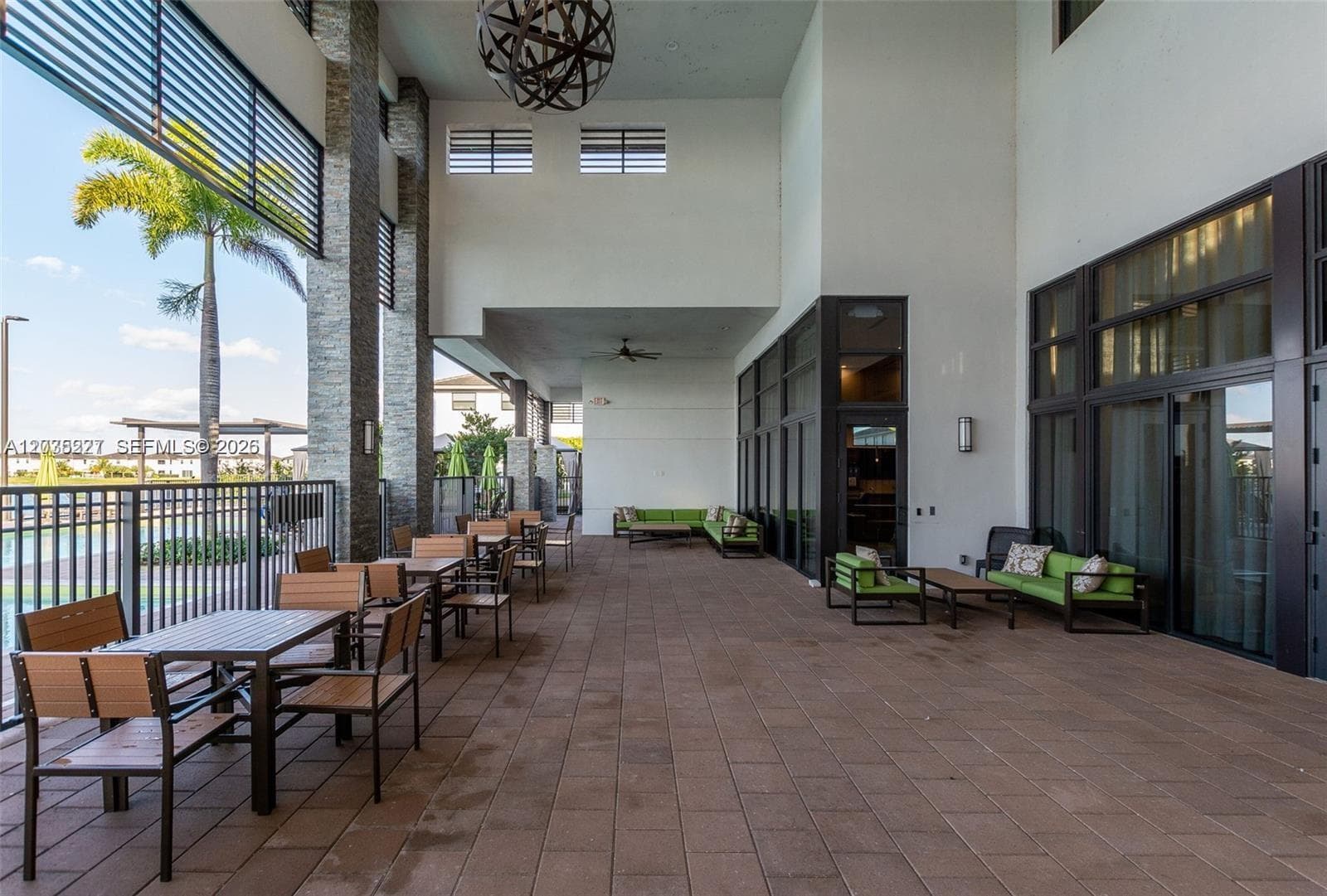 Expansive covered terrace with poolside views, offering both dining and lounge seating for residents to enjoy. A striking sphere chandelier and stacked-stone columns add architectural flair to this resort-style outdoor space.