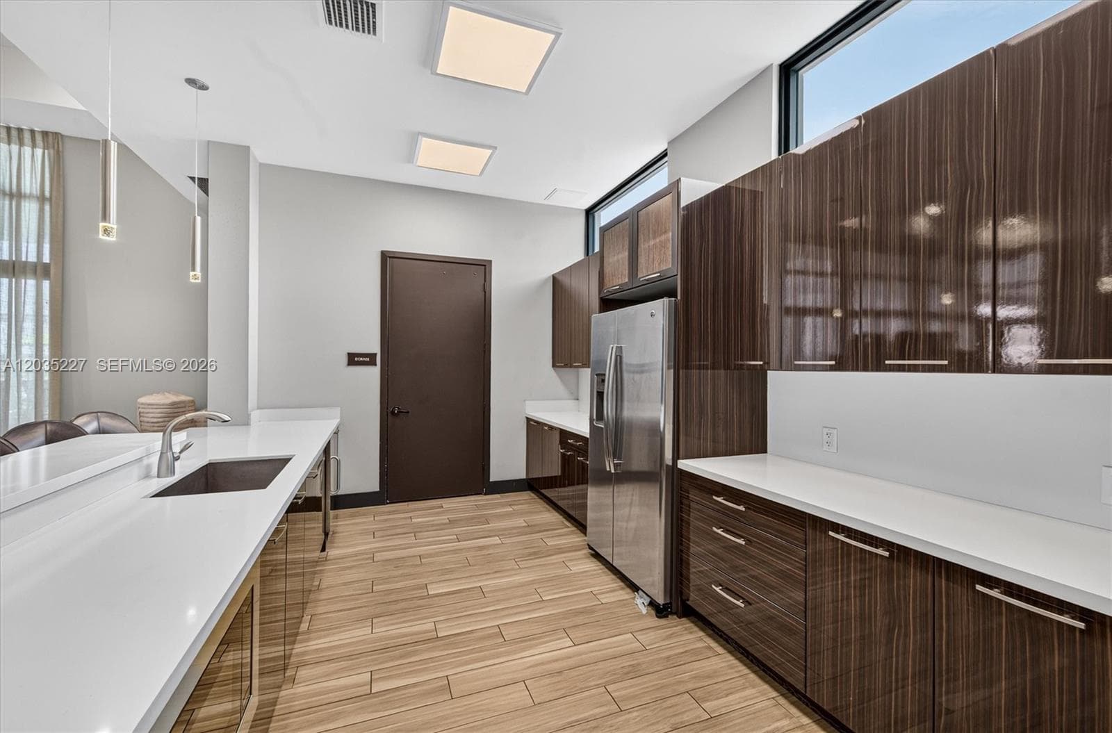 Elegant community kitchen with high-gloss espresso cabinetry and quartz countertops throughout. Floating pendant lights, transom windows, and a full stainless refrigerator make this a polished, functional space for residents.