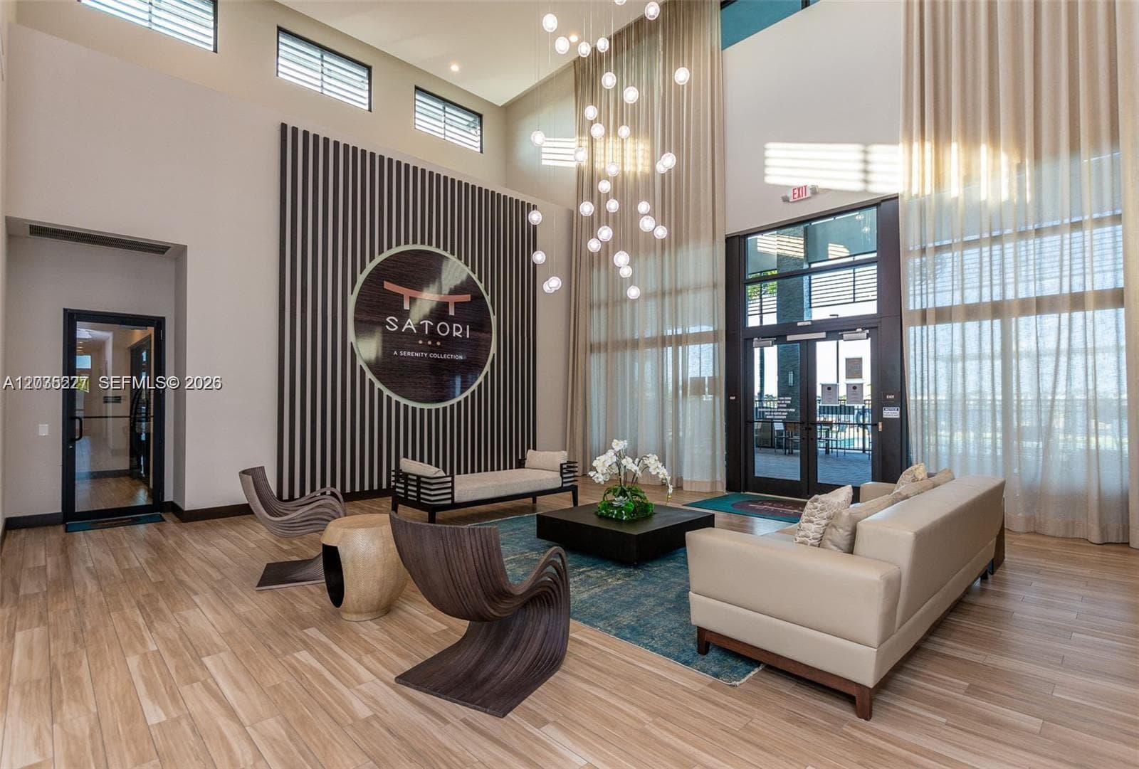 Soaring two-story lobby showcasing a dramatic bubble-light fixture and sculptural designer seating. Floor-to-ceiling sheer drapes and a striking signature wall create a sophisticated, hotel-like first impression.