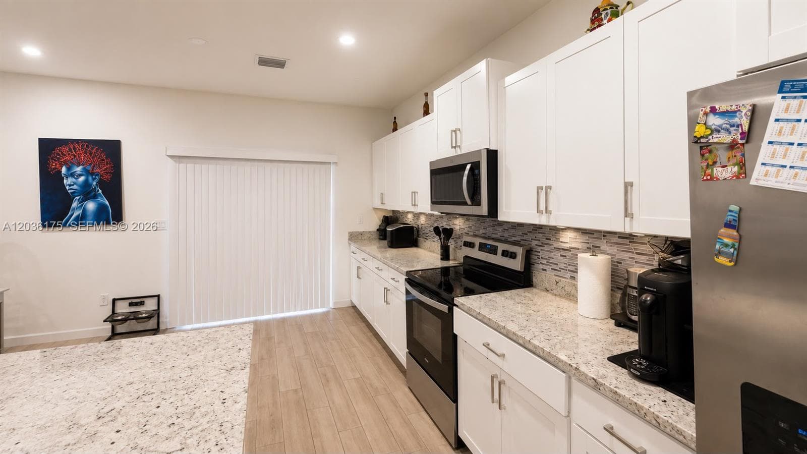 Kitchen featuring white cabinetry, stone countertops, stainless steel appliances, a tile backsplash, and wood-finish flooring