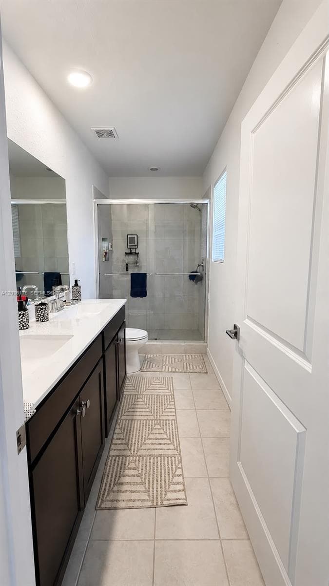 Double vanity with dark cabinetry, white countertops, glass-enclosed shower, and tile flooring
