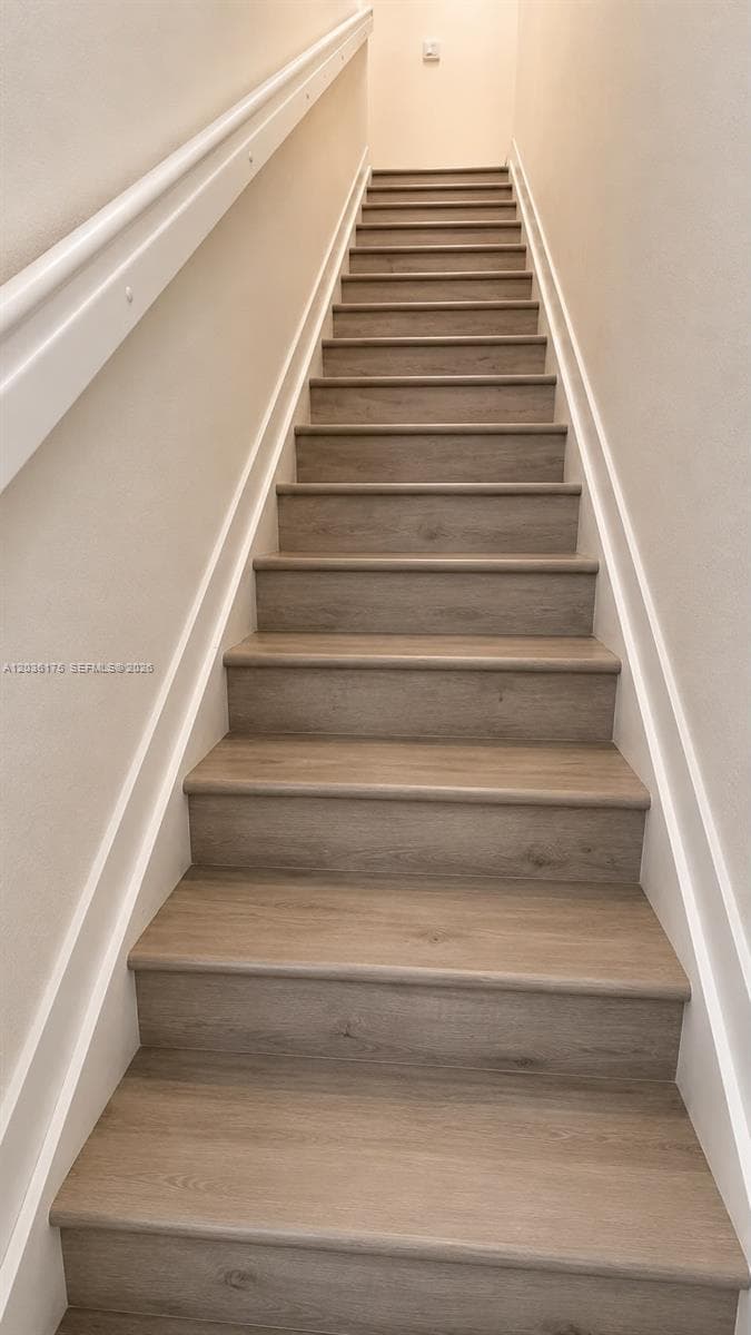 Staircase featuring wood-finish treads and a wall-mounted handrail